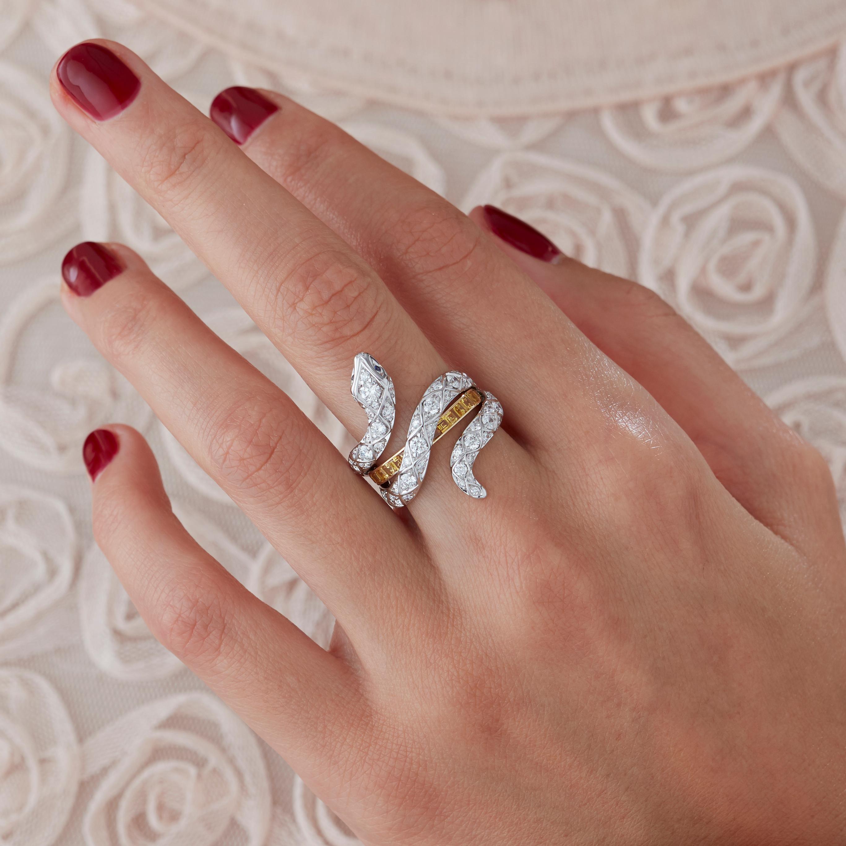 A House of Garrard 18 karat white gold 'Signature Serpent' ring from the 'Muse' collection, set with round white diamonds, round blue sapphires and calibre cut yellow sapphires.

67 round white diamonds weighing: 1.77cts 
2 round blue sapphires