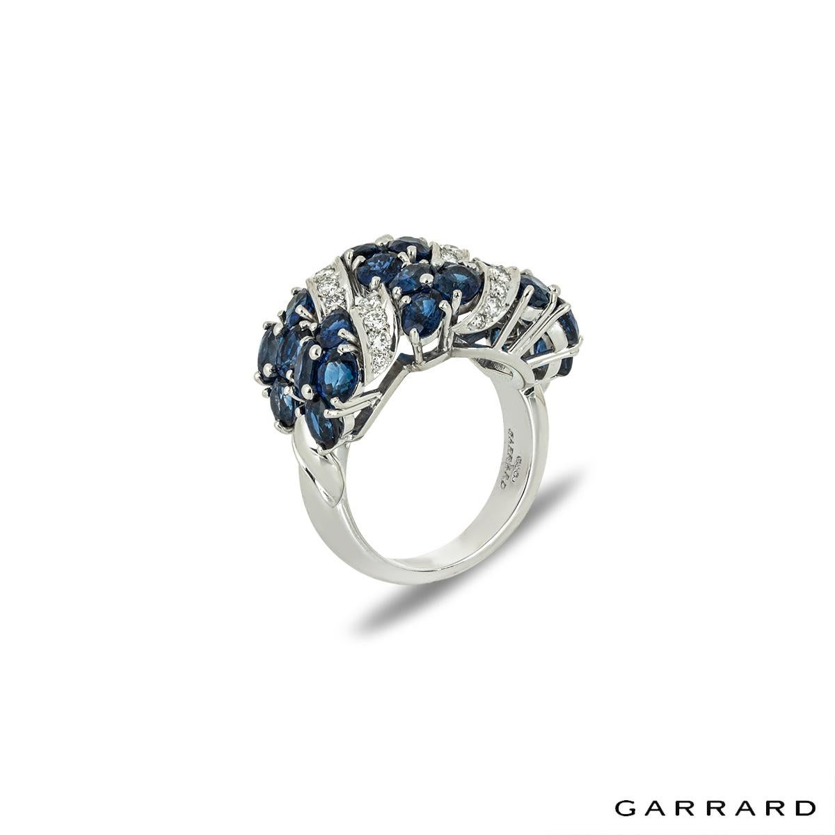An intricate 18k white gold sapphire and diamond ring by Garrard. The two-row ring alternates between sapphires and diamonds. The 24 oval cut sapphires have an approximate total weight of 5.52ct and display a rich blue hue. Pave set between the