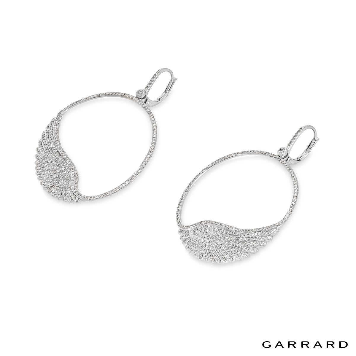 A spectacular pair of white gold diamond earrings by Garrard from the Wings Classic collection. The earrings each feature a diamond set half hoop that leads to a diamond set circular motif with an angel wing talisman at the bottom. The 564 round