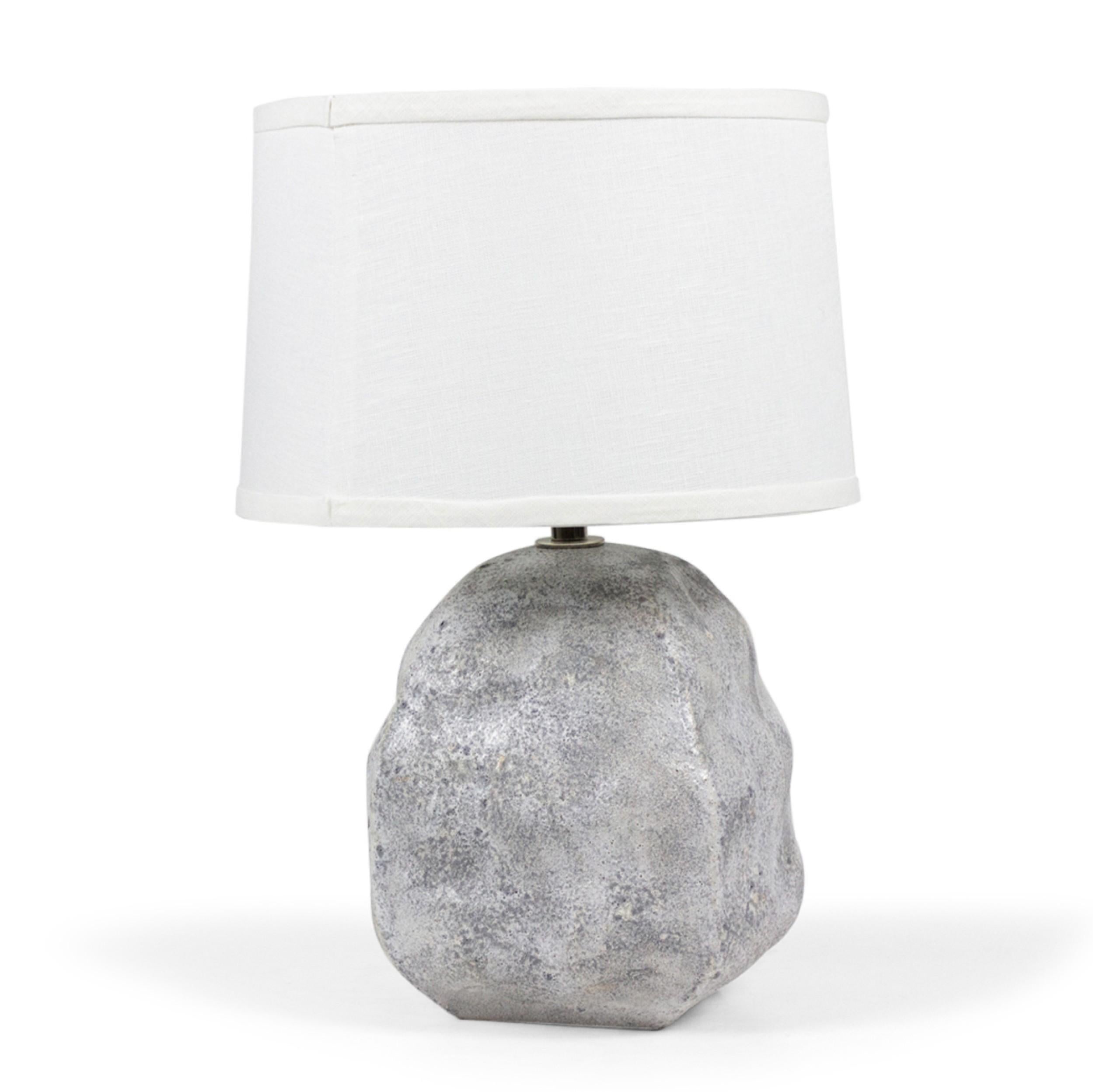 Contemporary ceramic table lamp with an organic bulbous form and and a gray textured surface, mounted with silver metal harp and hardware supporting a beige drum shade. (GARY DIPASQUALE)