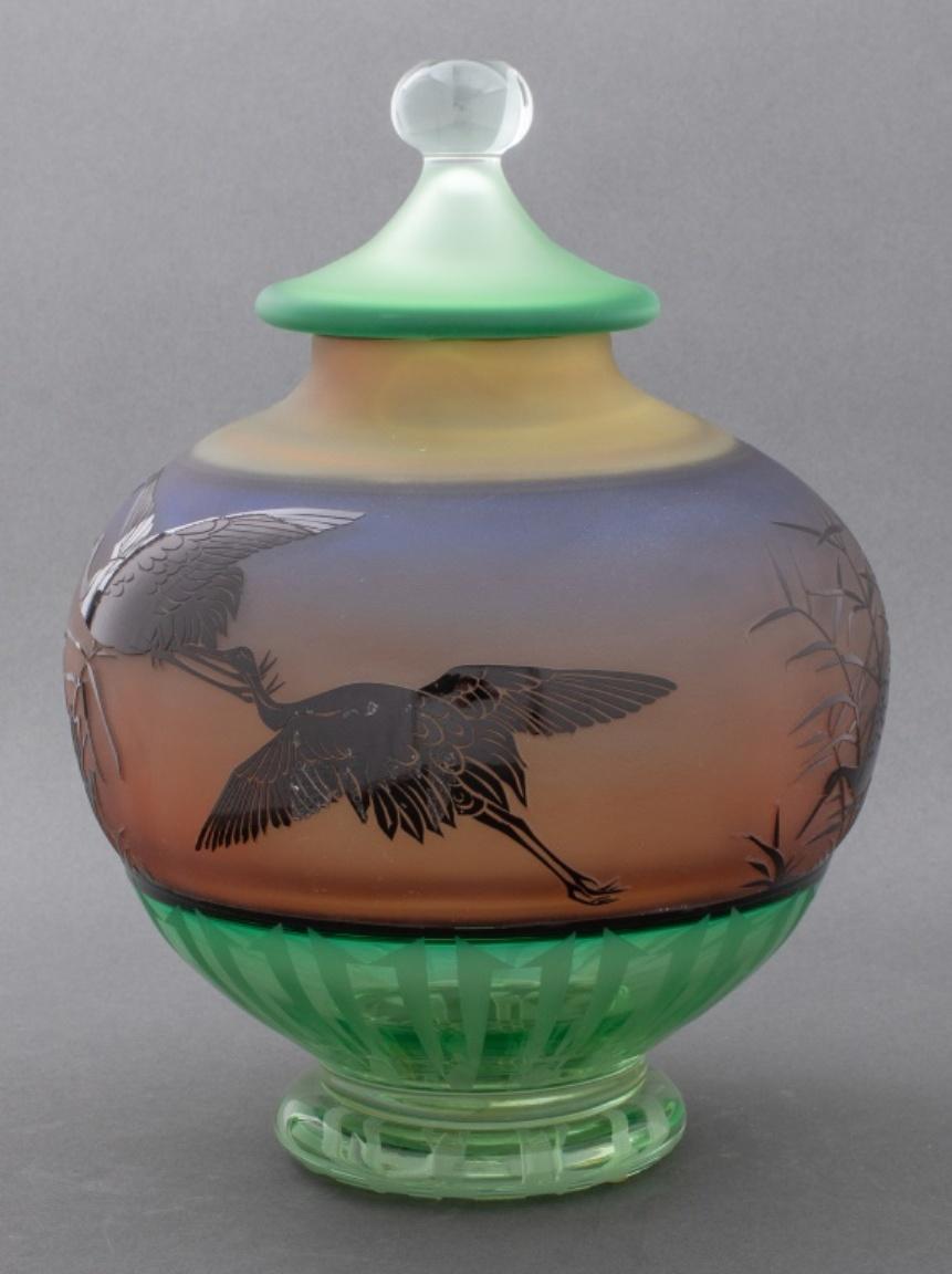 Gary Genetti (American, b. 1953) studio art glass covered vase with acid etched decoration and black cut to polychrome cameo design comprising a heron crane bird motif, the frosted green glass lid with spherical colorless glass finial, the foot with