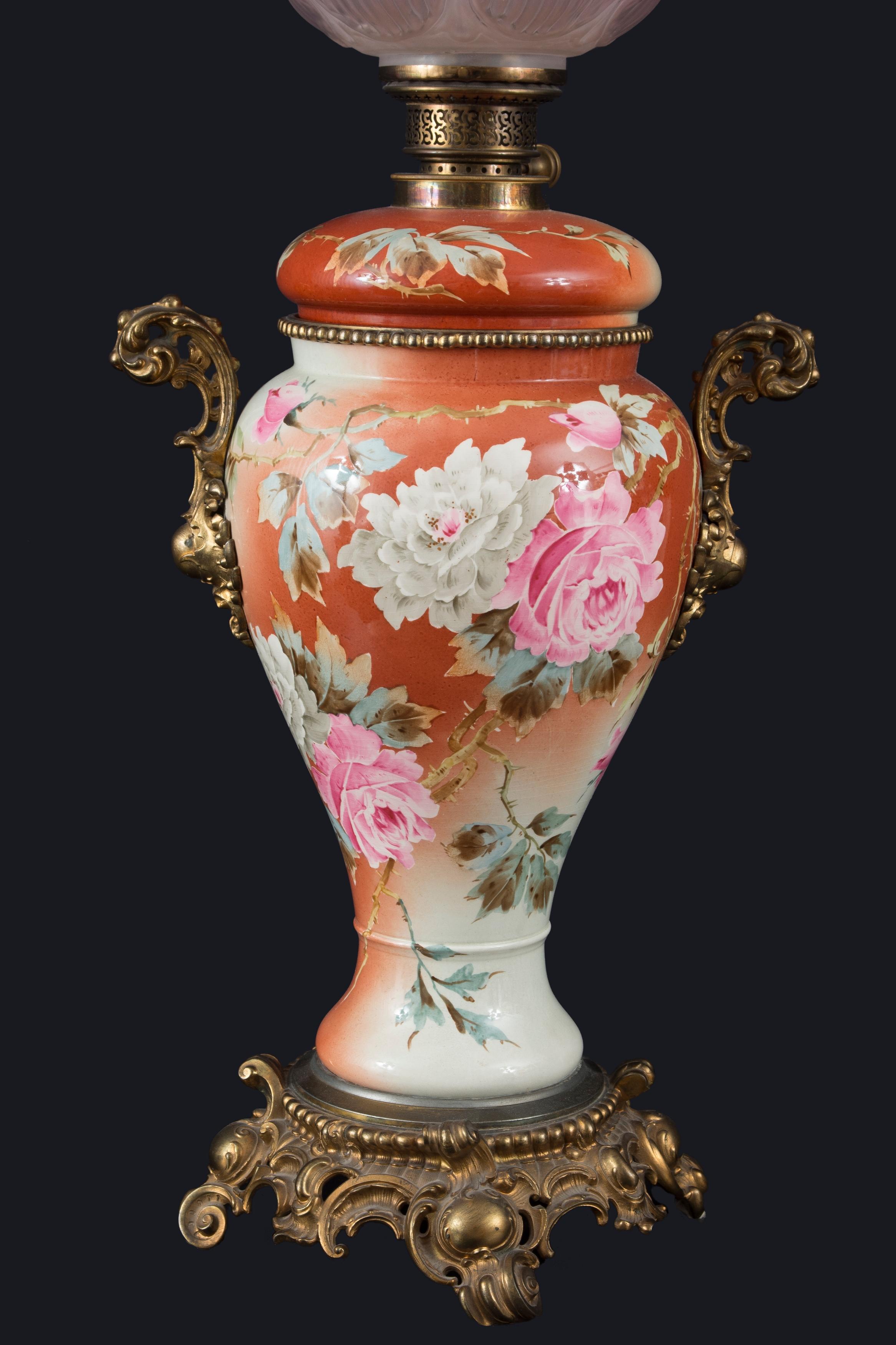 Lampe à gaz en verre, bronze doré et porcelaine émaillée, XIXe siècle.
Un piédestal avec rocailles et médaillons sert de base au vase en porcelaine décoré de roses qui constitue le corps de la lampe, et comporte deux poignées en métal. La partie