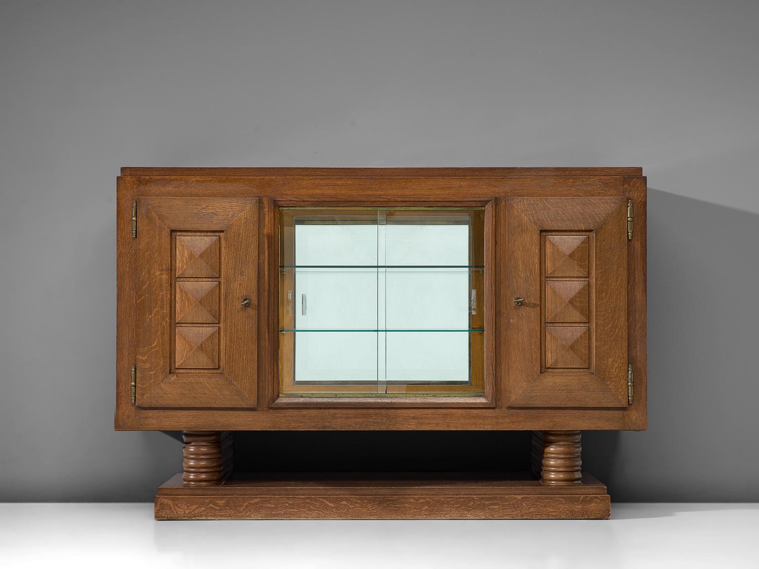 Gaston Poisson, credenza, stained oak, mirror and glass, France 1930s. 

Sturdy credenza in oak with graphical doorpanels and glass middle section. This sideboard is equipped with several shelves which provide plenty of storage space. The shelves
