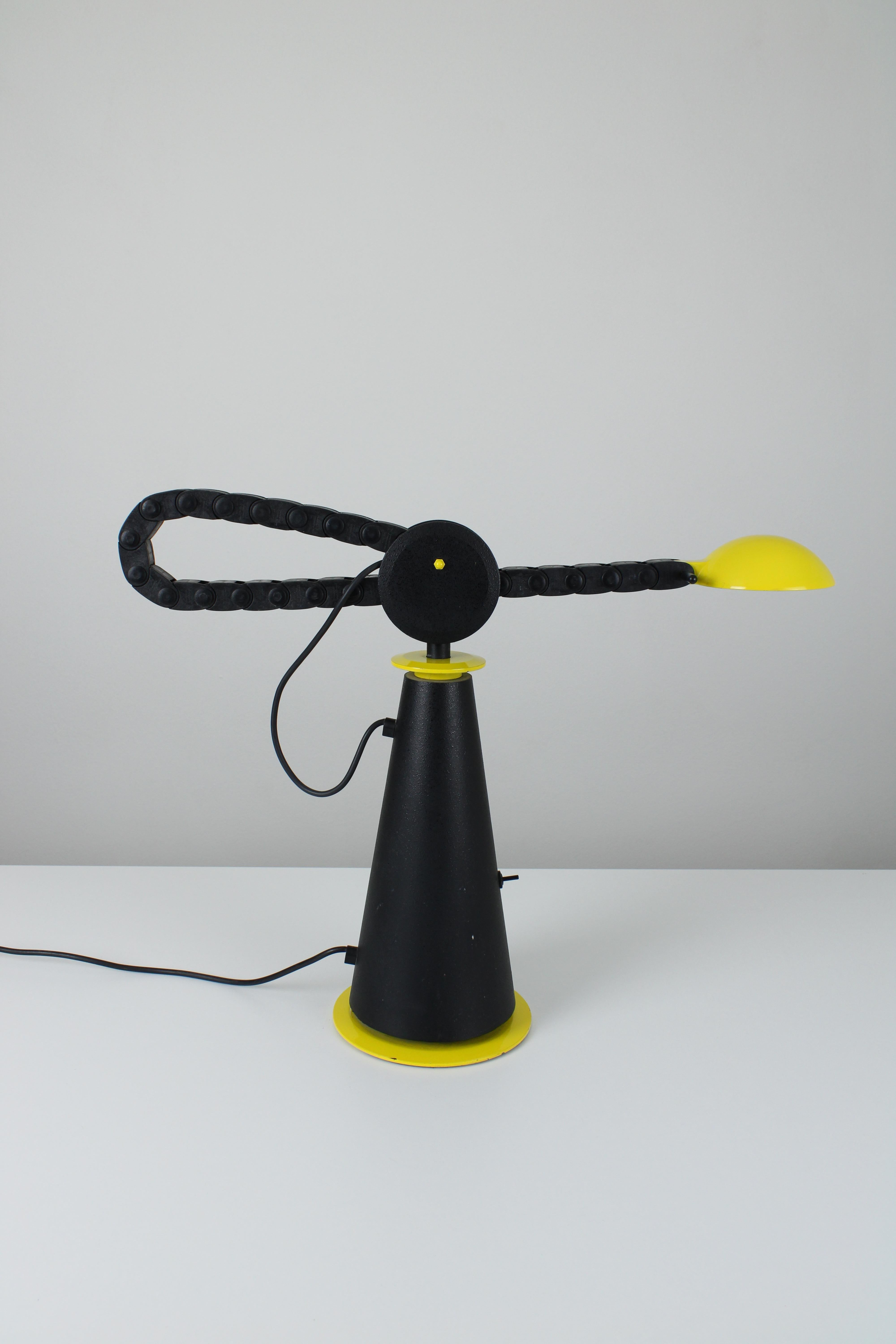 Table lamp, model Gaucho. Designed by Studio PER for Egoluce in 1982.
This lamp is made of a heavy steel base that holds a bicycle chain like adjustable arm. That makes it possible to easily extend the arm horizontally. On the base is a light