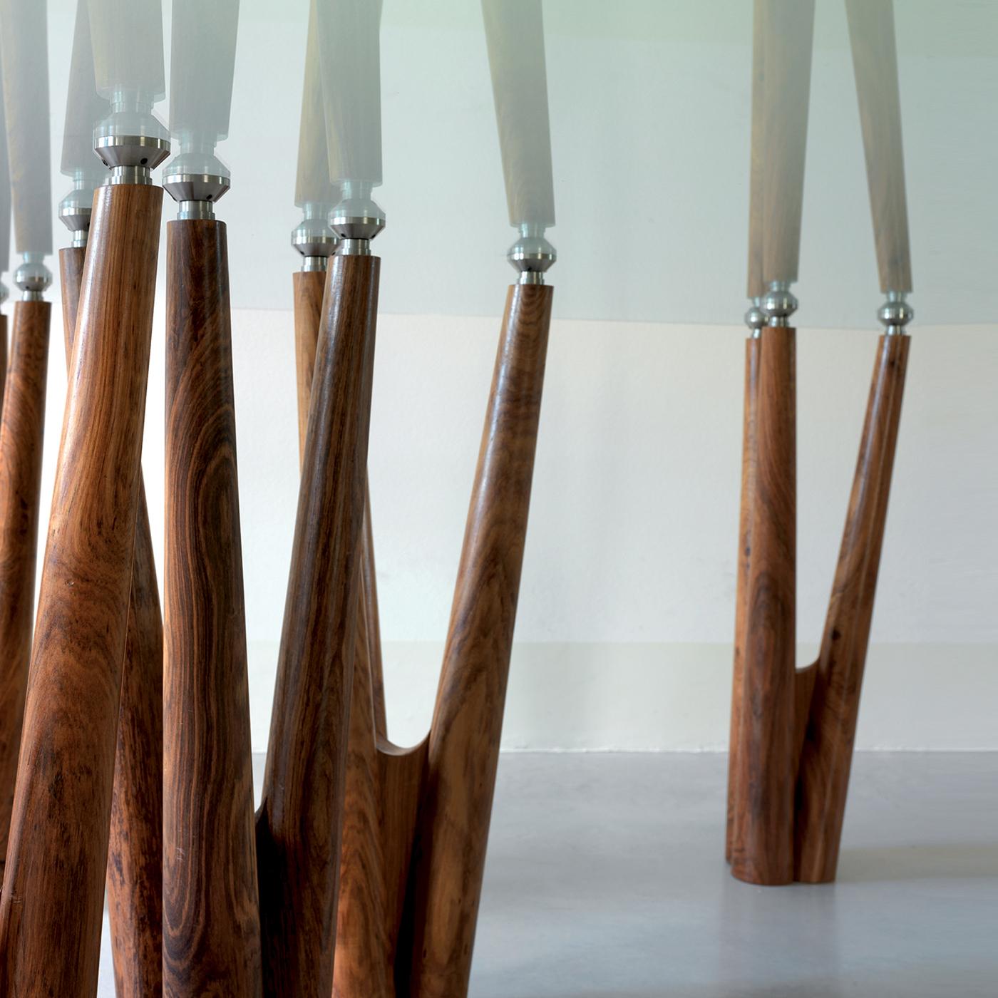 La table Gaudi est un hommage au grand maître. Dans chaque base, les pièces appartiennent au même arbre, de sorte que les grains et les couleurs continuent à jouer et à donner un feuillage tout à fait artificiel. Les bases en palissandre massif sont