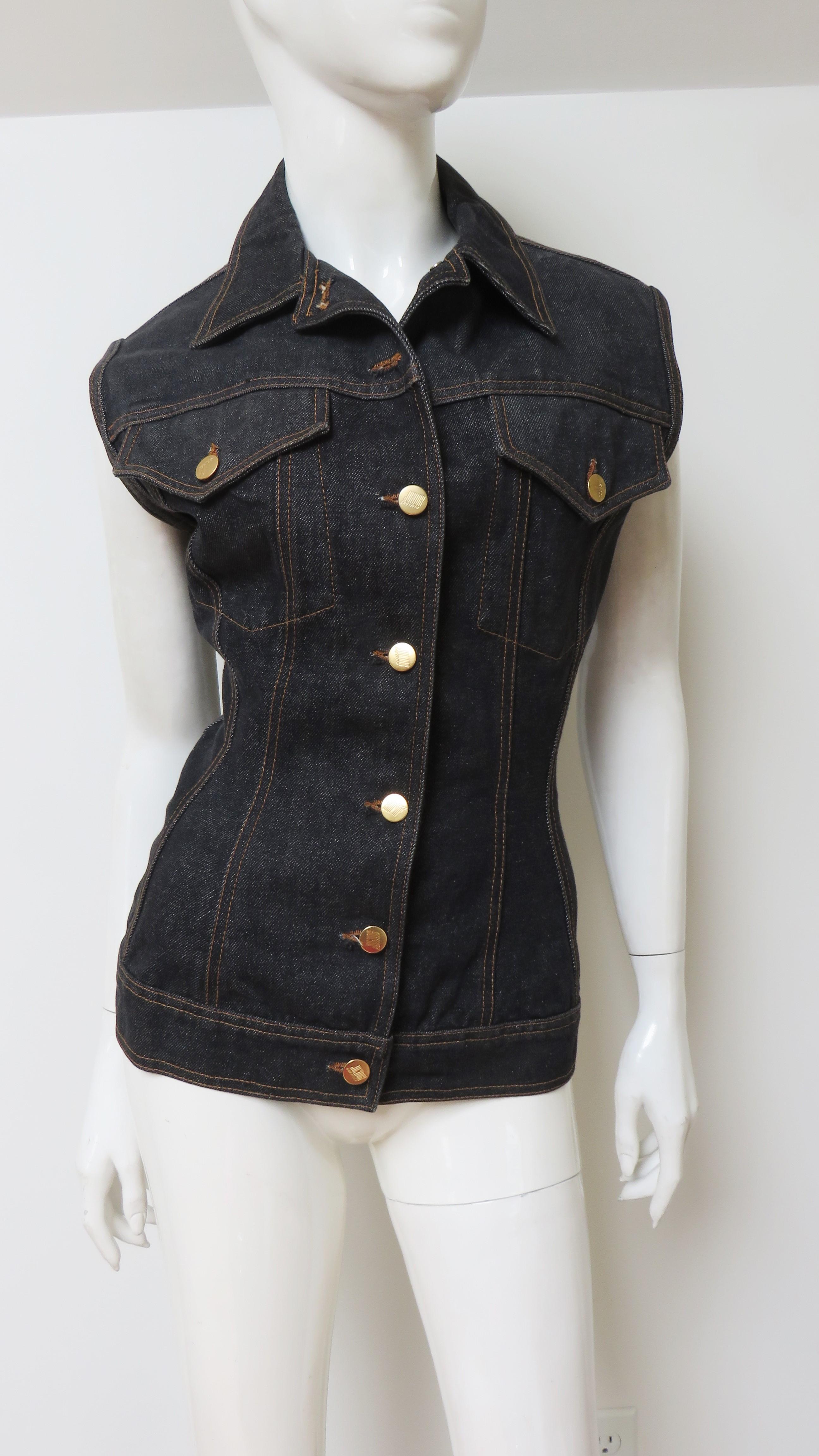 Un fantastico gilet ispirato alla giacca di jeans blu navy della linea Jean Paul Gaultier Junior.  Presenta bottoni metallici dorati con scritte Gaultier sul davanti, sulle tasche applicate e sui fianchi.  È aderente e regolabile con un'allacciatura