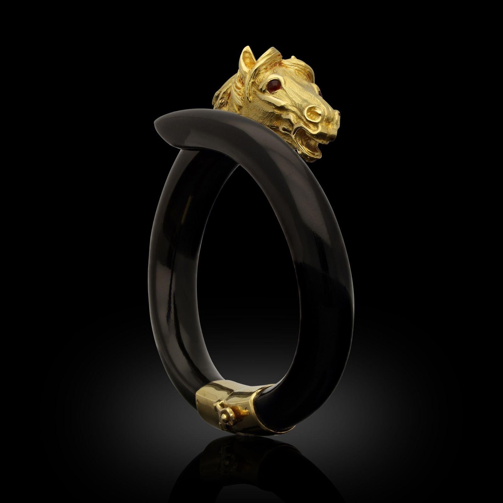 An 18ct gold and wooden stallion’s head bangle by Gay Freres c.1970s, the open by-pass style bangle fashioned from smoothly carved and polished ebony wood with one tapering end and the other set with an 18ct yellow gold stallion’s head with mane