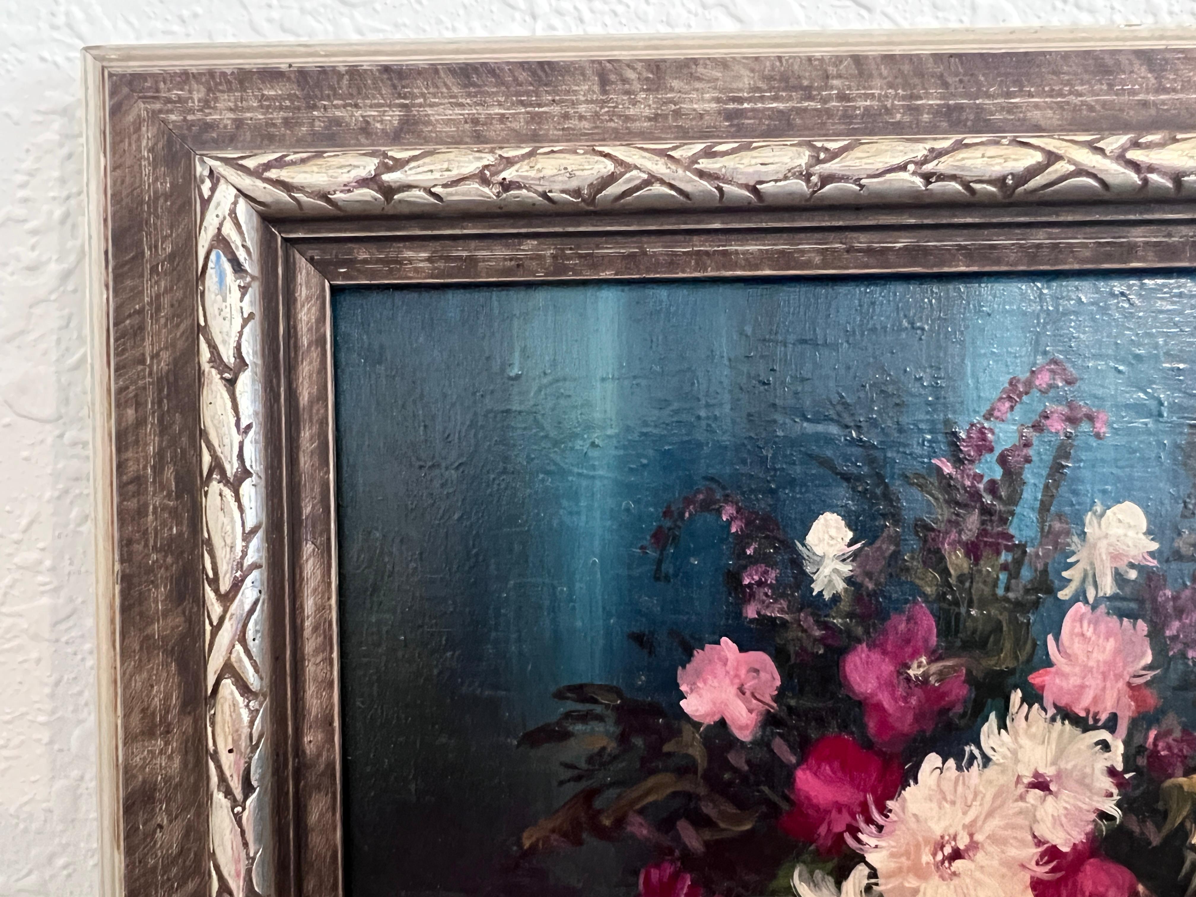 Este pequeño óleo vintage sobre tabla es una composición clásica de bodegón en la que aparece un ramo de flores en un jarrón, acompañado de una elegante jarra de metal y un pequeño objeto decorativo. Las flores, pintadas en tonos rosa, blanco y rojo