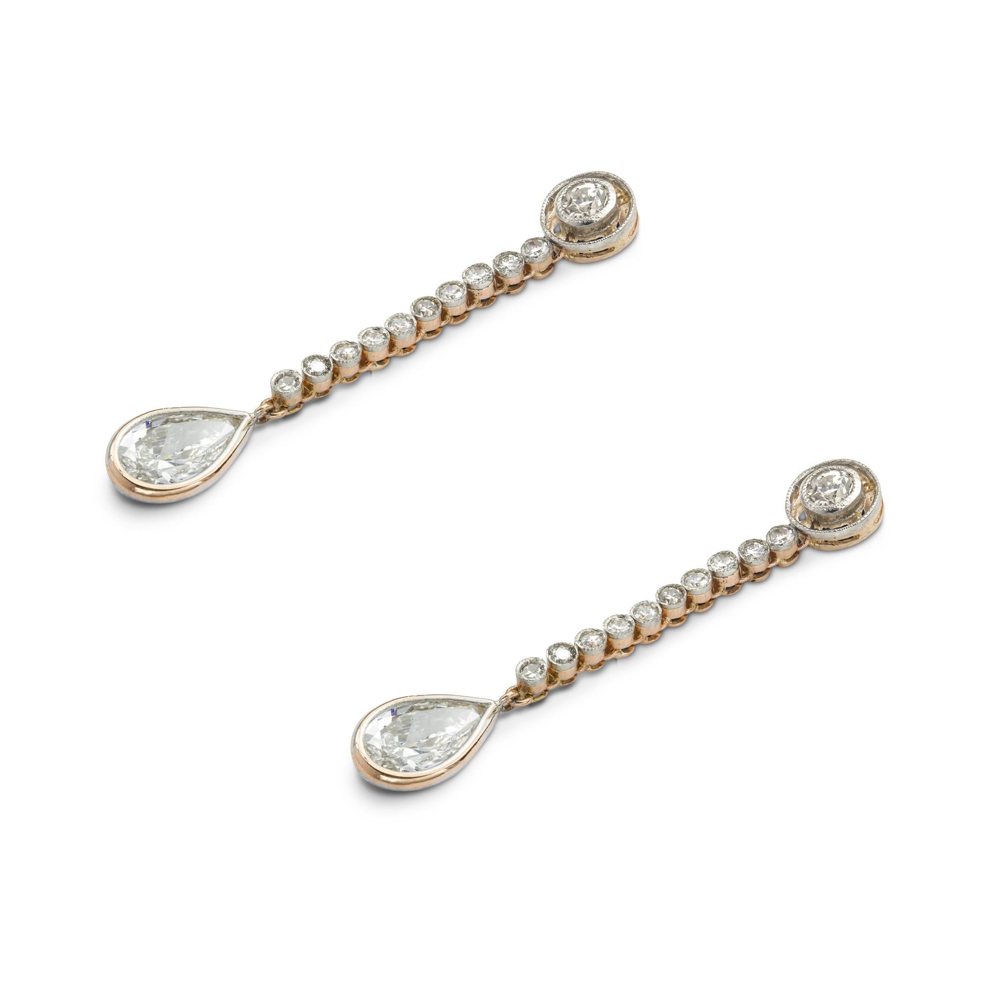 Un paio di orecchini con diamanti a goccia, la parte superiore incastonata con un diamante vecchio taglio brillante all'interno di un'aureola millegradi che conduce a una linea di diamanti fino a un diamante a forma di pera in un'incastonatura a