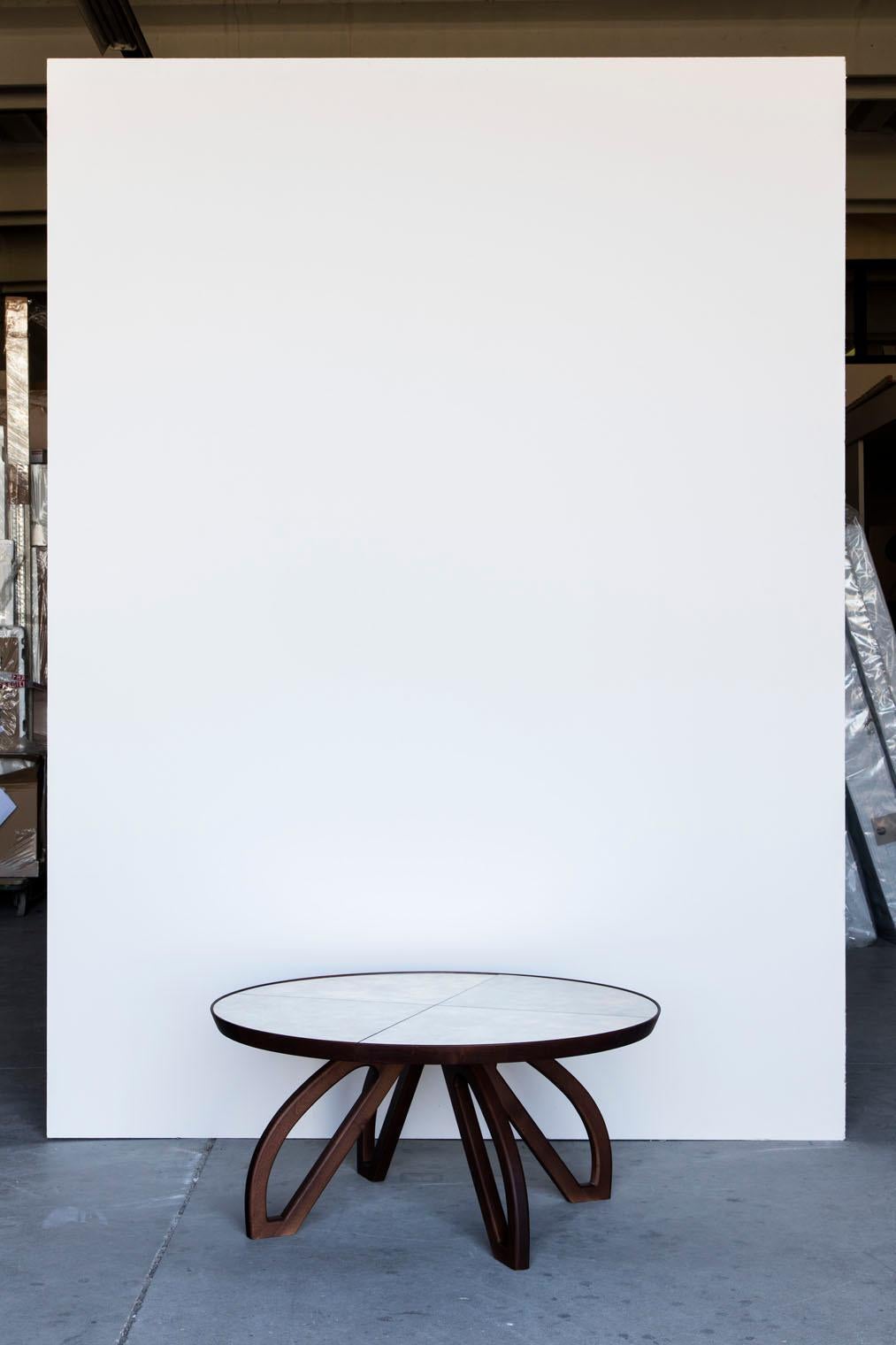 A round sofa table with a twist, the elegant wooden legs open up towards the floor like a flower. The table top is covered with four pieces of antiquated mirrors.