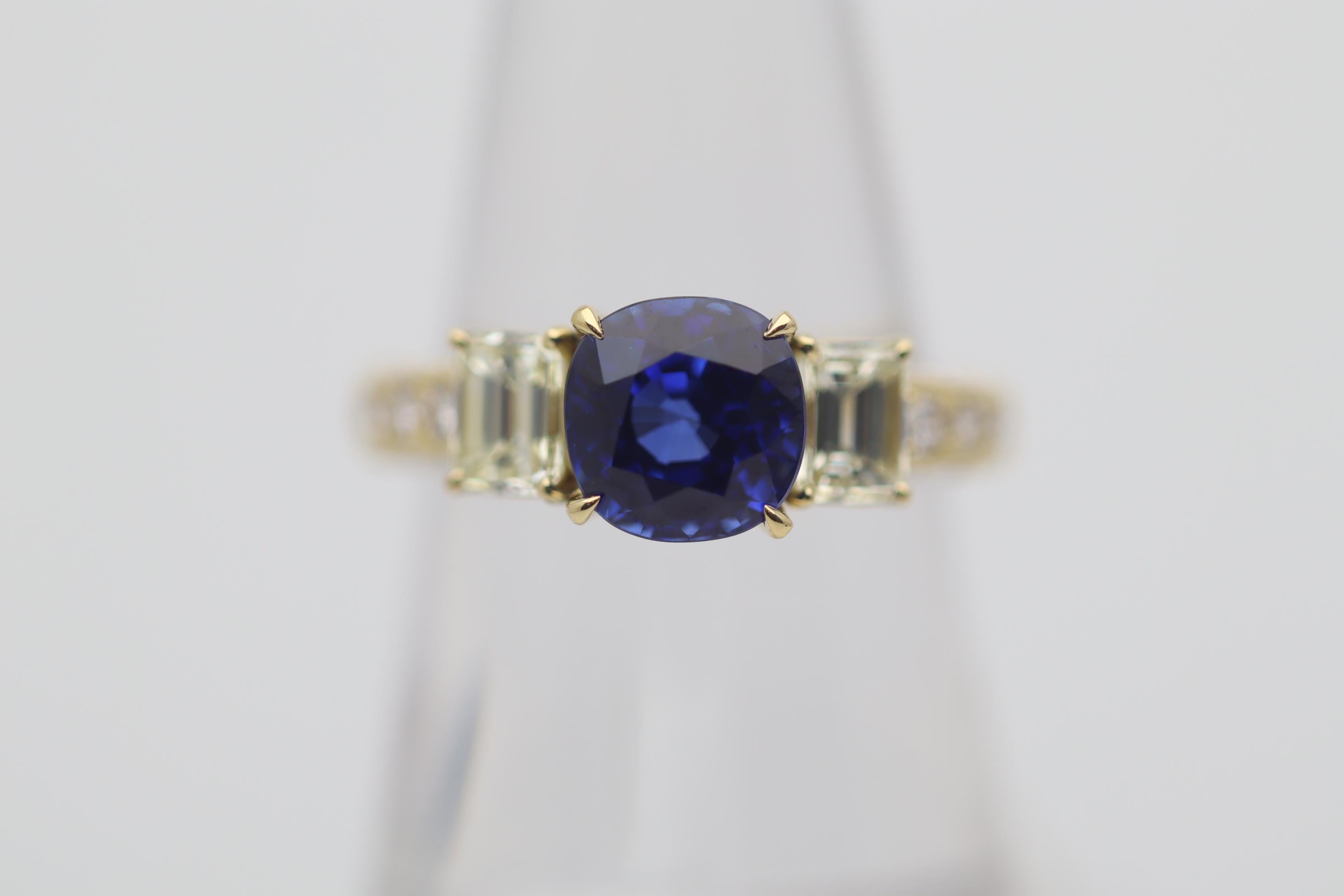 A superb sapphire weighing a respectable 2.86 carats takes center stage of this gold and diamond ring. The sapphire has a bright rich electric blue color with excellent scintillation. It is complemented by two emerald-cut diamonds set on its sides