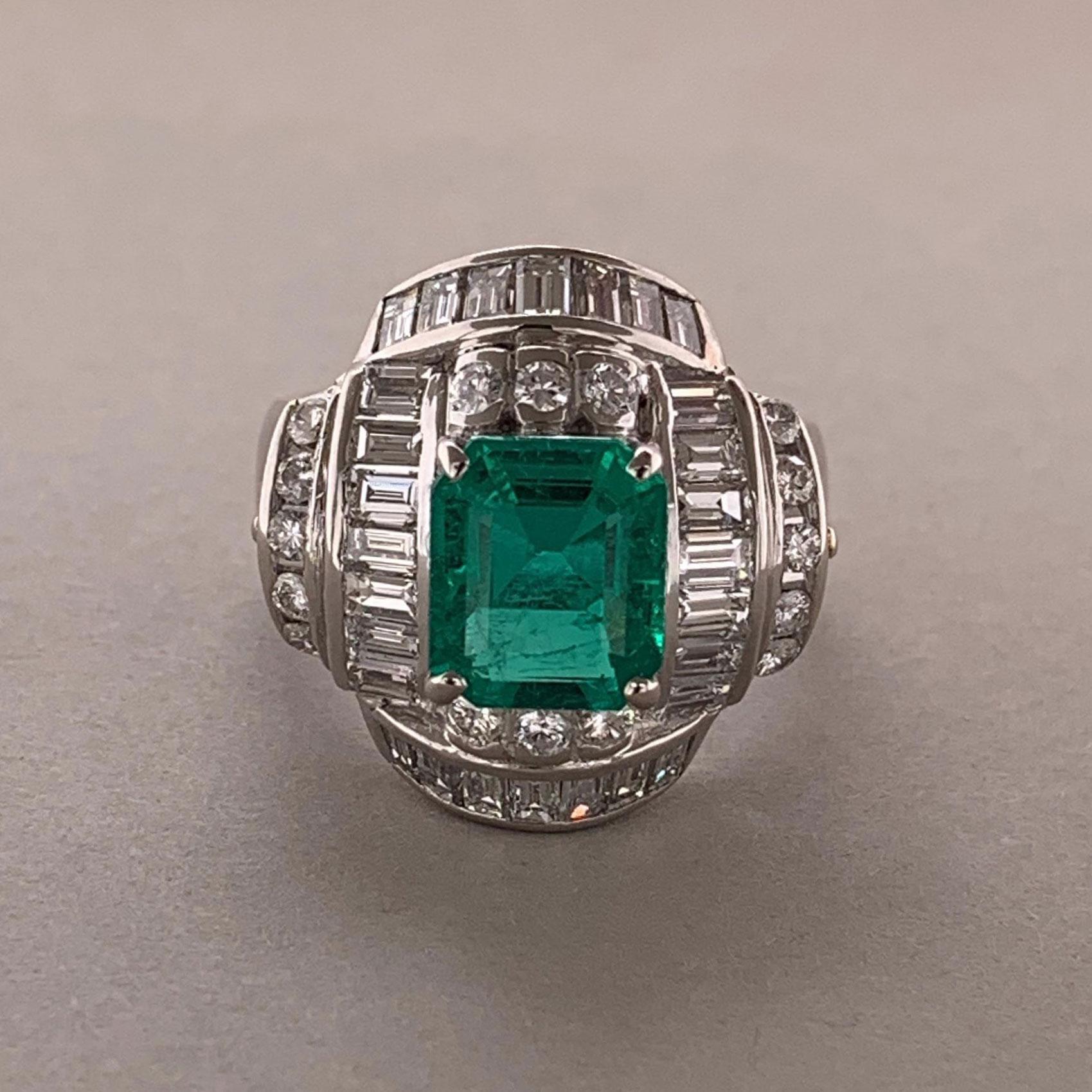 A superb gem quality emerald sits proudly atop this platinum ring. It weighs 2.47 carats and has a bright vivid green color while being free of any noticeable inclusions commonly found in emeralds. It is accompanied by 2.23 carats of round brilliant