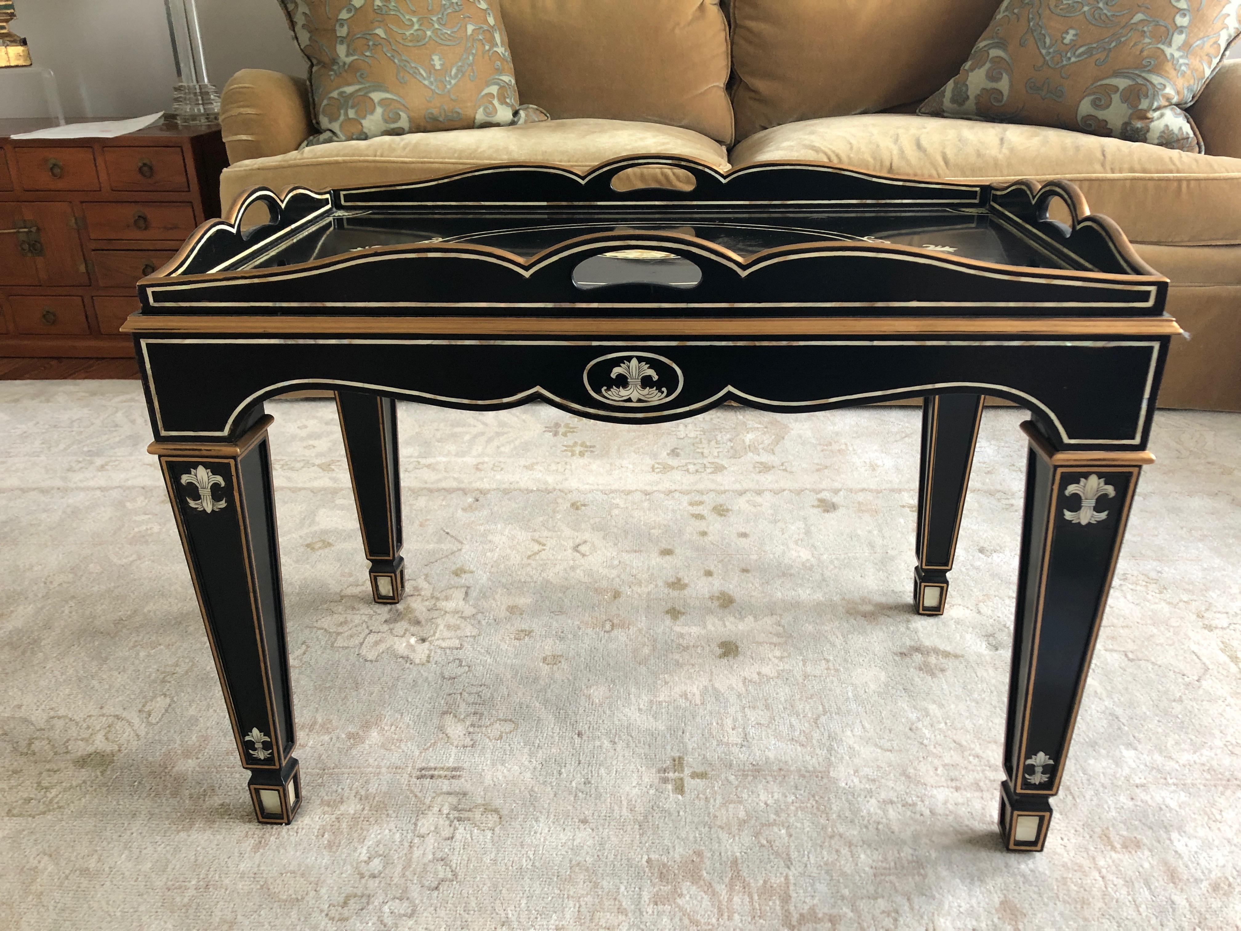 Very elegant small rectangular tray coffee table having a black background and gorgeous mother of pearl and gold decoration including inlay central medallion, border and corner embellishments and fleur di lis like designs on the tapered legs,