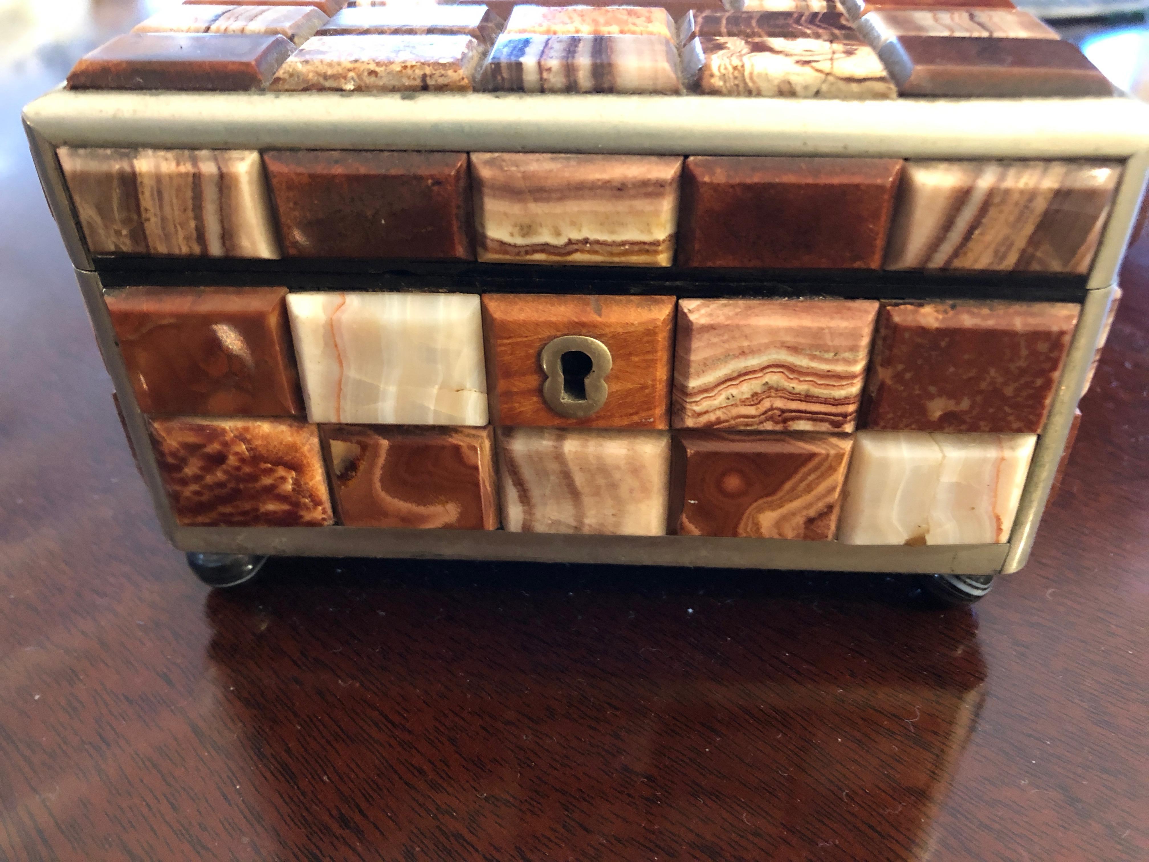 A gorgeous antique trinket box encrusted with small rectangles of earth colored agates & marble, including brown, orange, cream, and gold. There is silver metal edging and a silver keyhole, lined in wood inside.