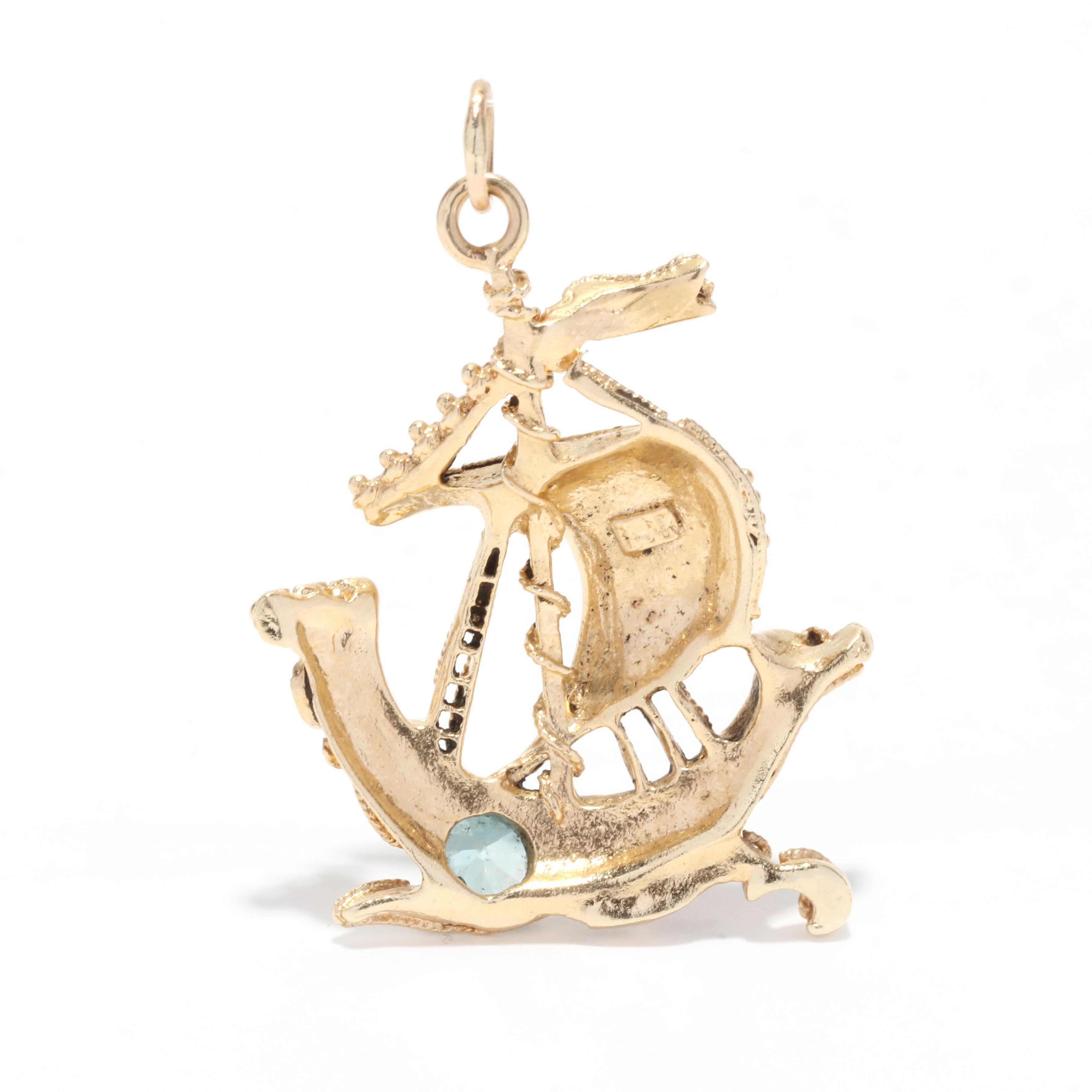 A mid-century 14 karat yellow gold gem-set viking ship charm. This medium size charm features a viking ship motif with applied gold swirl detailing and set with gemstones such as blue zircon, coral and colored glass stones.

Stones: 
- blue zircon,
