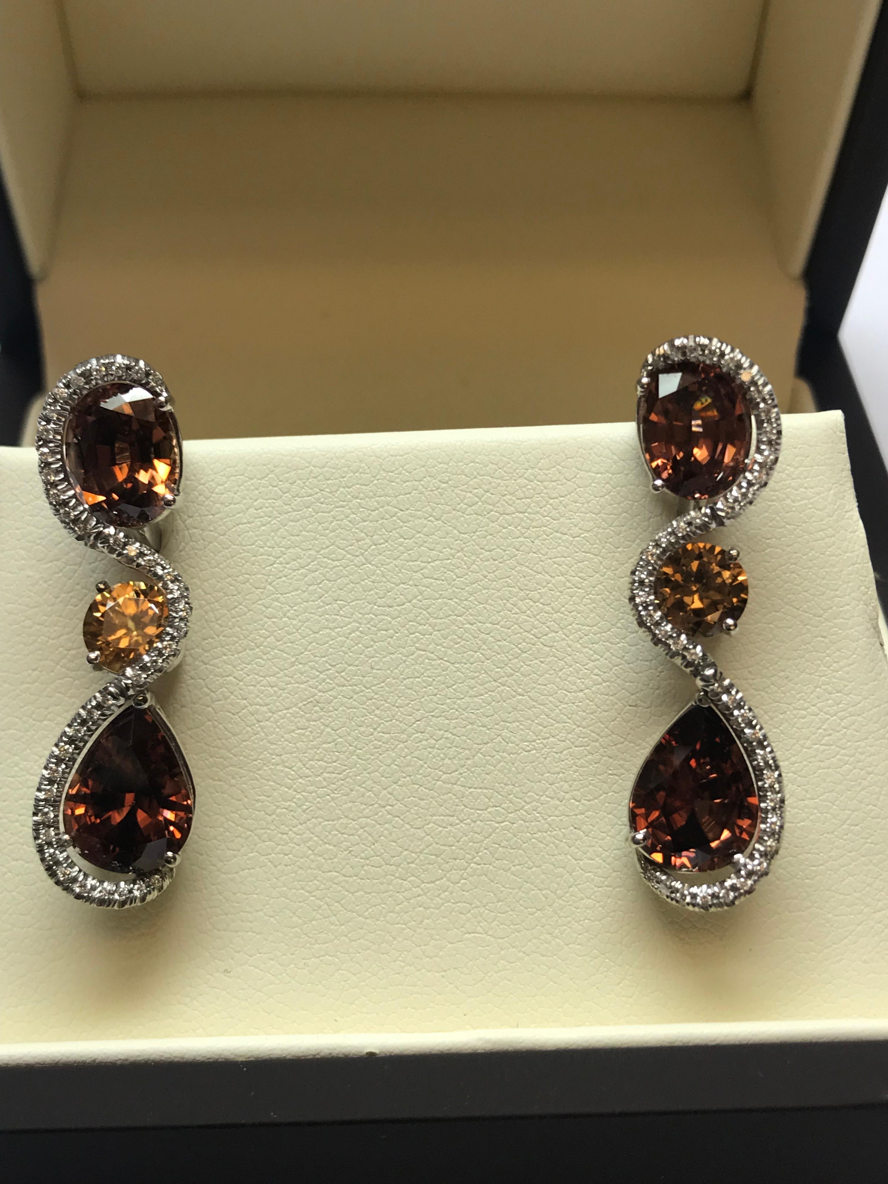 The fire in these very unique colored Tanzanian Zircon earrings surrounded by white diamonds really are a show stopper. The 12.55 carats in total weight of oval, round and pear shaped Zircons are accented perfectly with diamonds and the design of