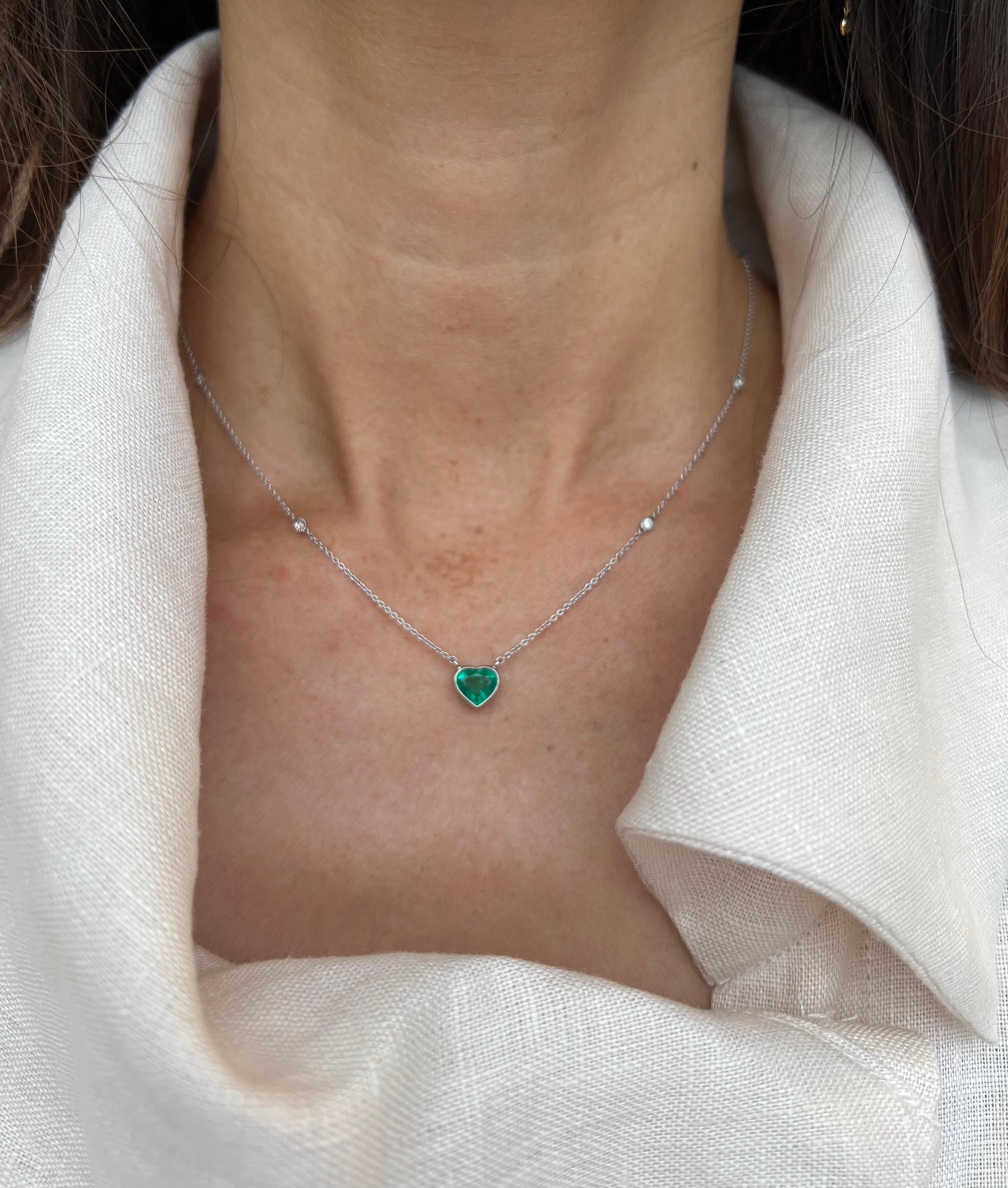 Striking vivid green heart-shaped emerald weighing 1.18 carat is at center of this beautiful and elegant necklace. It is set in fine bezel. The platinum cable link chain is decorated with 8 round brilliant cut diamonds encircled with milgrain