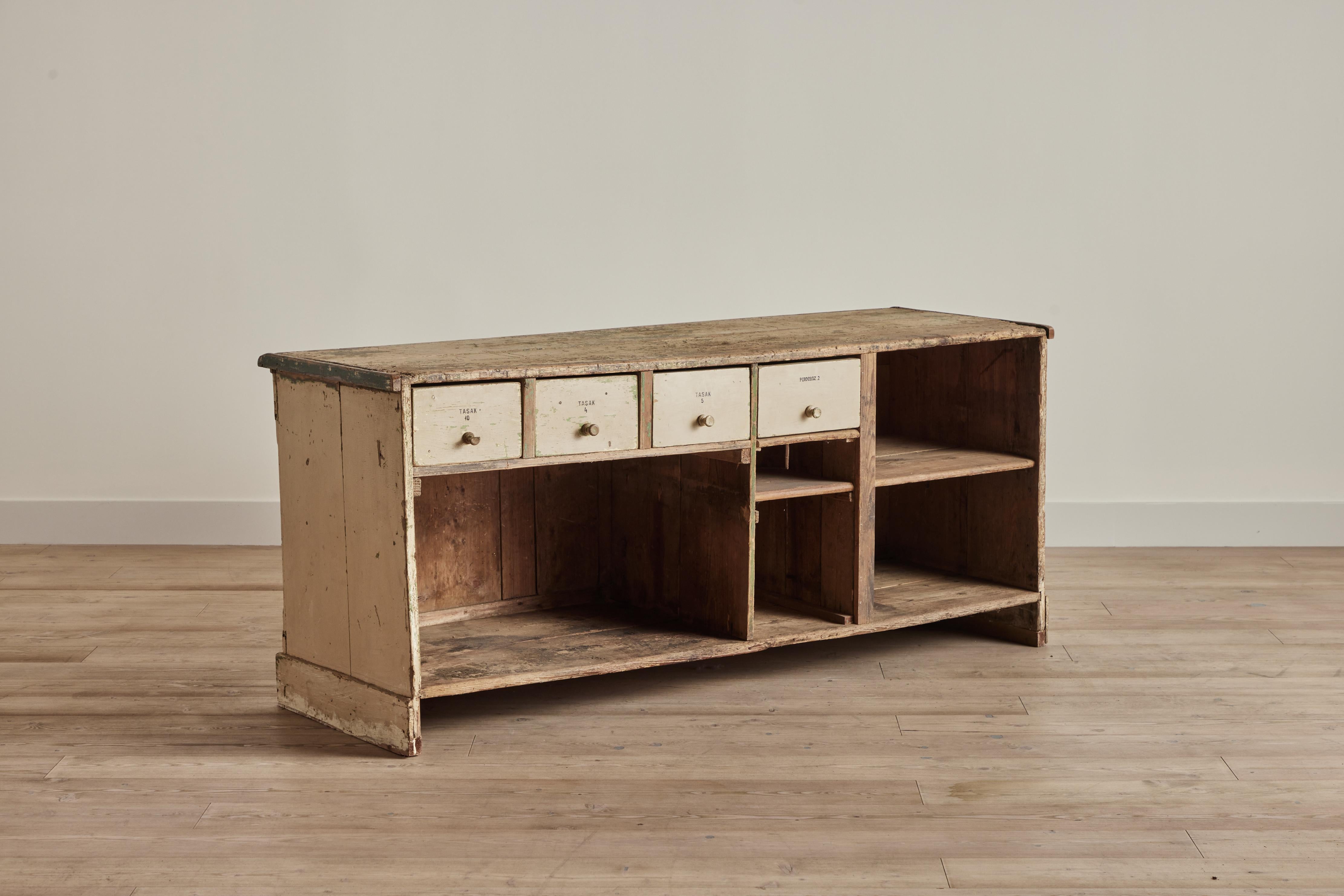 Rustic general store shop counter with four drawers and shelving, United States circa 1900. Heavy wear throughout on painted yellow finish and wood. 