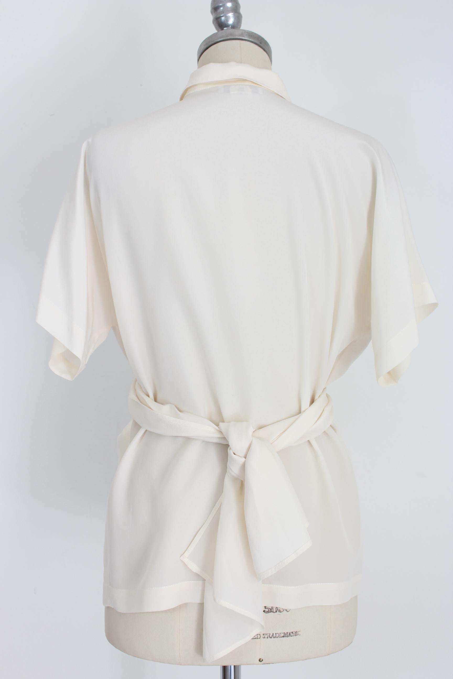 Genny by Gianni Versace 80s vintage women's shirt. Short model at the waist, soft belt closure at the waist. V-shaped neckline, short sleeves. Beige color, 100% silk. Made in Italy. Very good vintage condition, some small imperfections due to