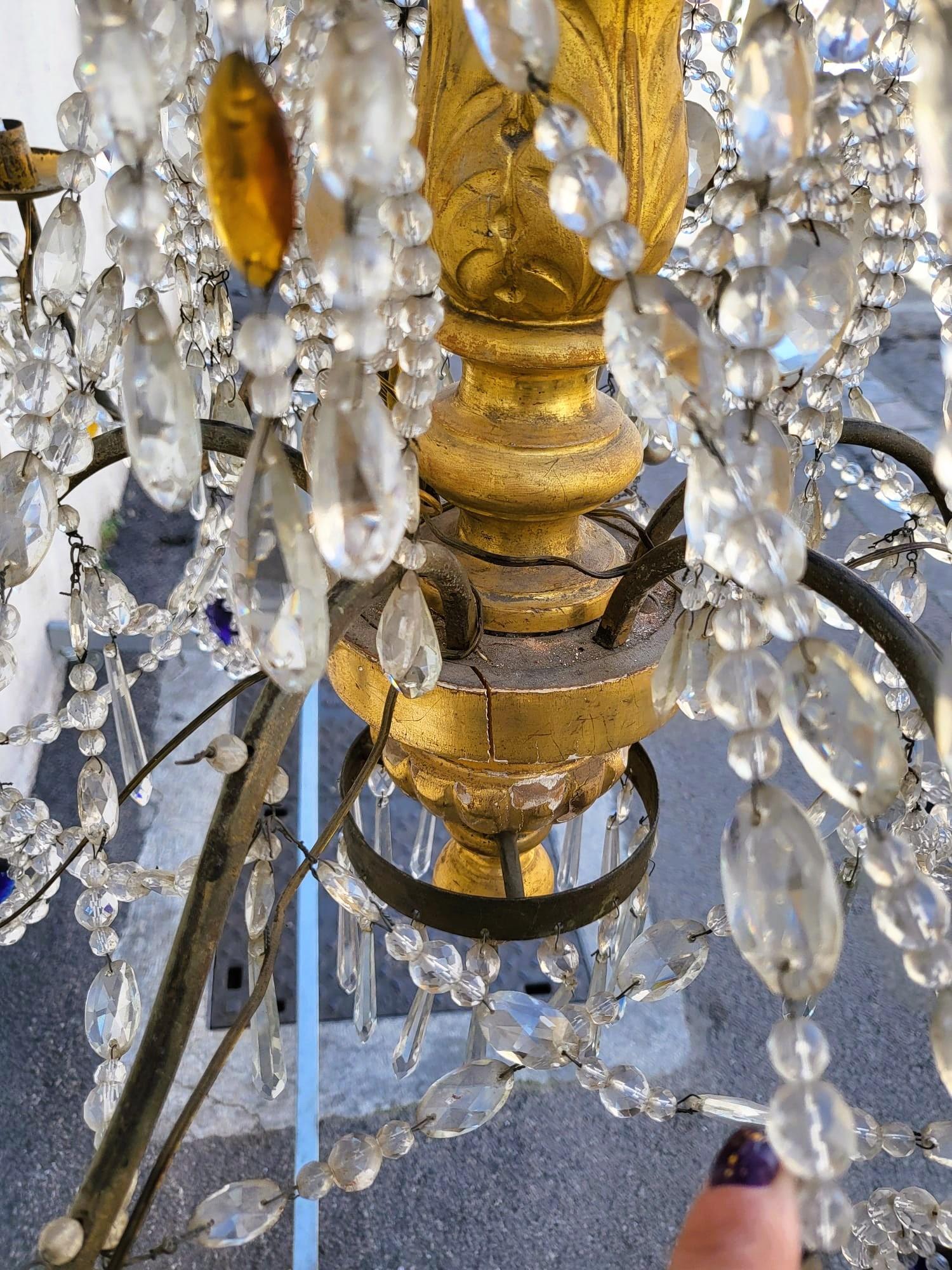 Grand lustre génois, en bois doré et pampilles de cristal, en guirlandes élégamment entrelacées, nuancées de couleurs (bleu et orange) fin 18e et début 19e siècle.

La tige centrale en bois est dorée, les 6 bras de lumière sont en fer.

Les lustres