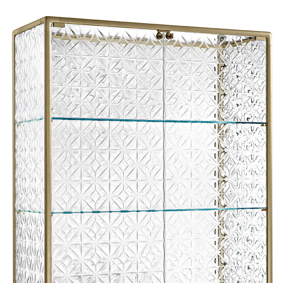 Glass Case Genova large with aluminum structure
in veneered brass finish. With fused carved clear glass
structure and doors, 6mm thickness. Inside tempered 
glass shelves in 8mm thickness. Each shelf can support 
20 kilos. Base in tempered