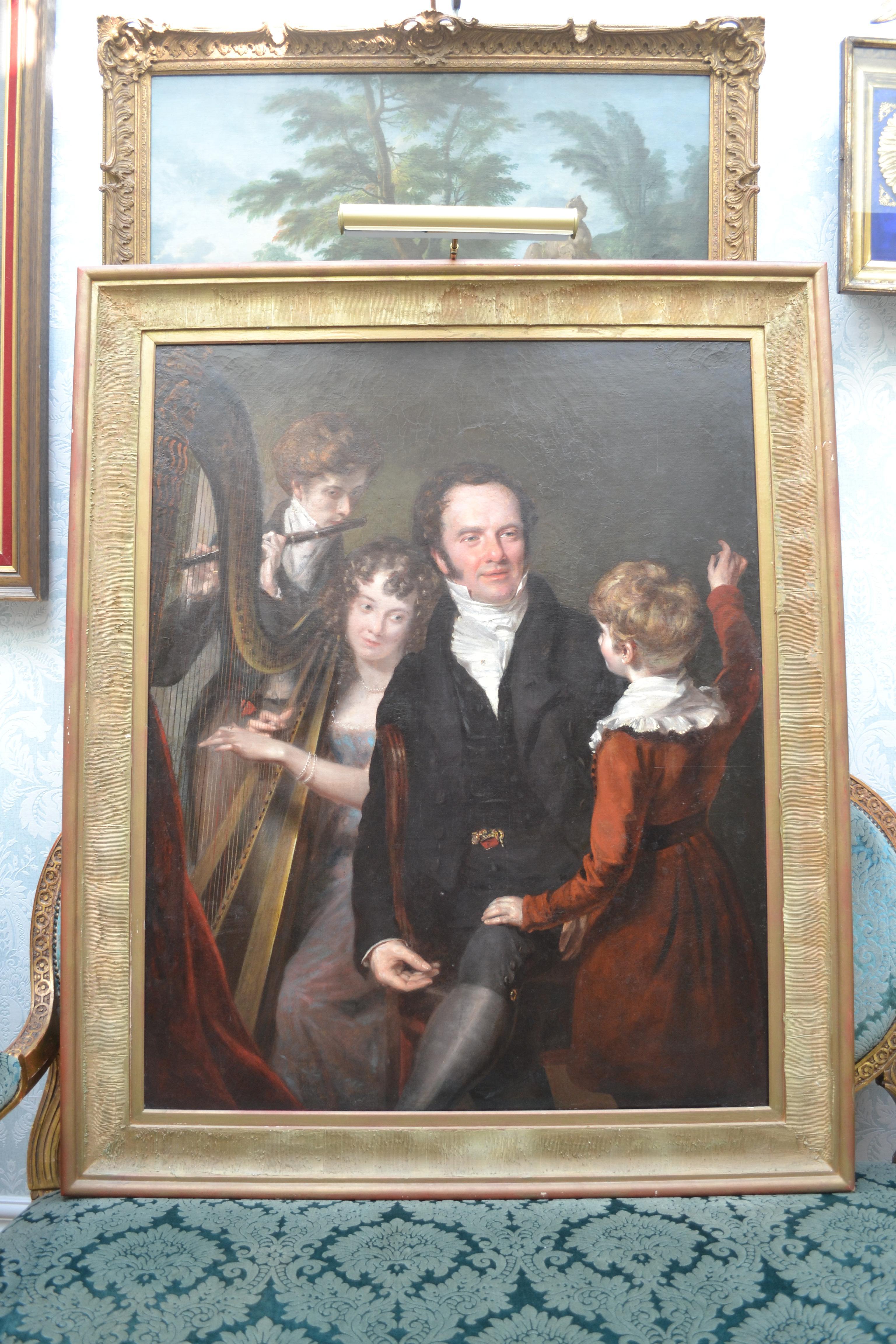 A large oil on canvas depicting a youthful father with his three children, two of which are behind him playing musical instruments, the daughter with her harp and son playing the flute. A third child with his back to the painter faces his father.