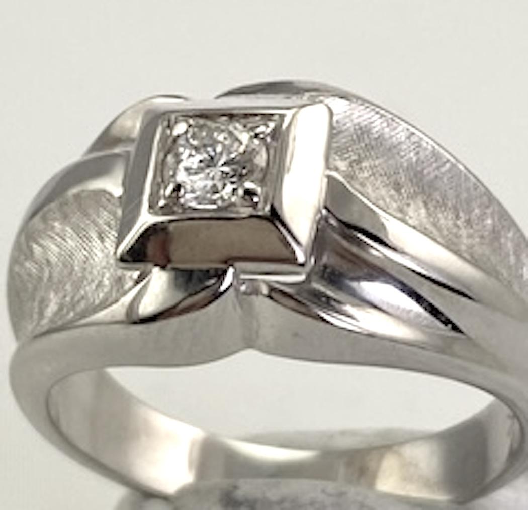 This gent's ring has a contemporary unique style and is constructed in 14 karat white gold. The round brilliant cut diamond set in a square top is .25 carat and I2; H quality. It was conservatively graded and measured by a GIA graduate gemologist.