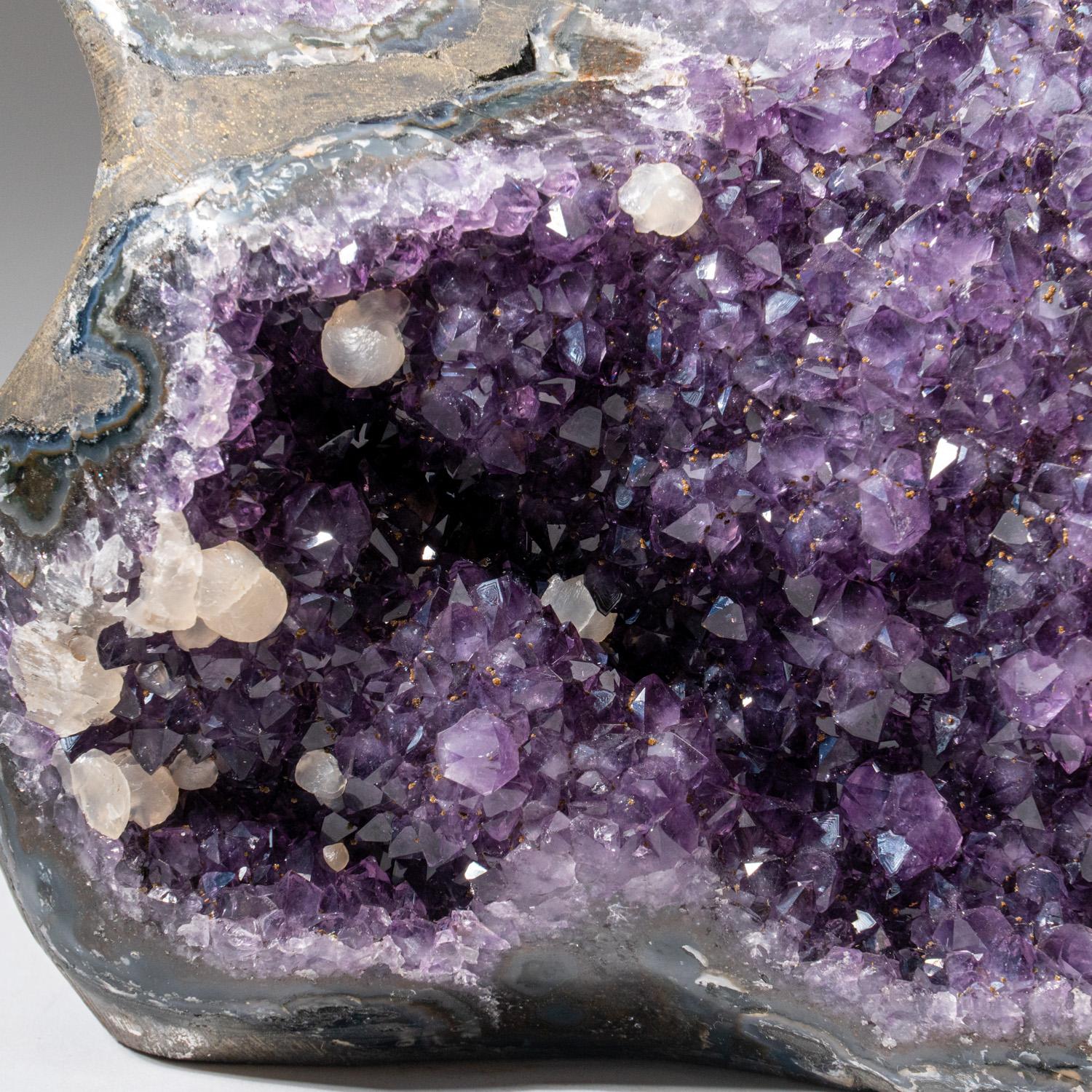 AAA-quality Amethyst cluster geode accented with several small calcite crystals. This specimen is lined with lustrous crystallized Amethyst variety quartz crystals, transparent to translucent, with deep grape purple color and highly reflective