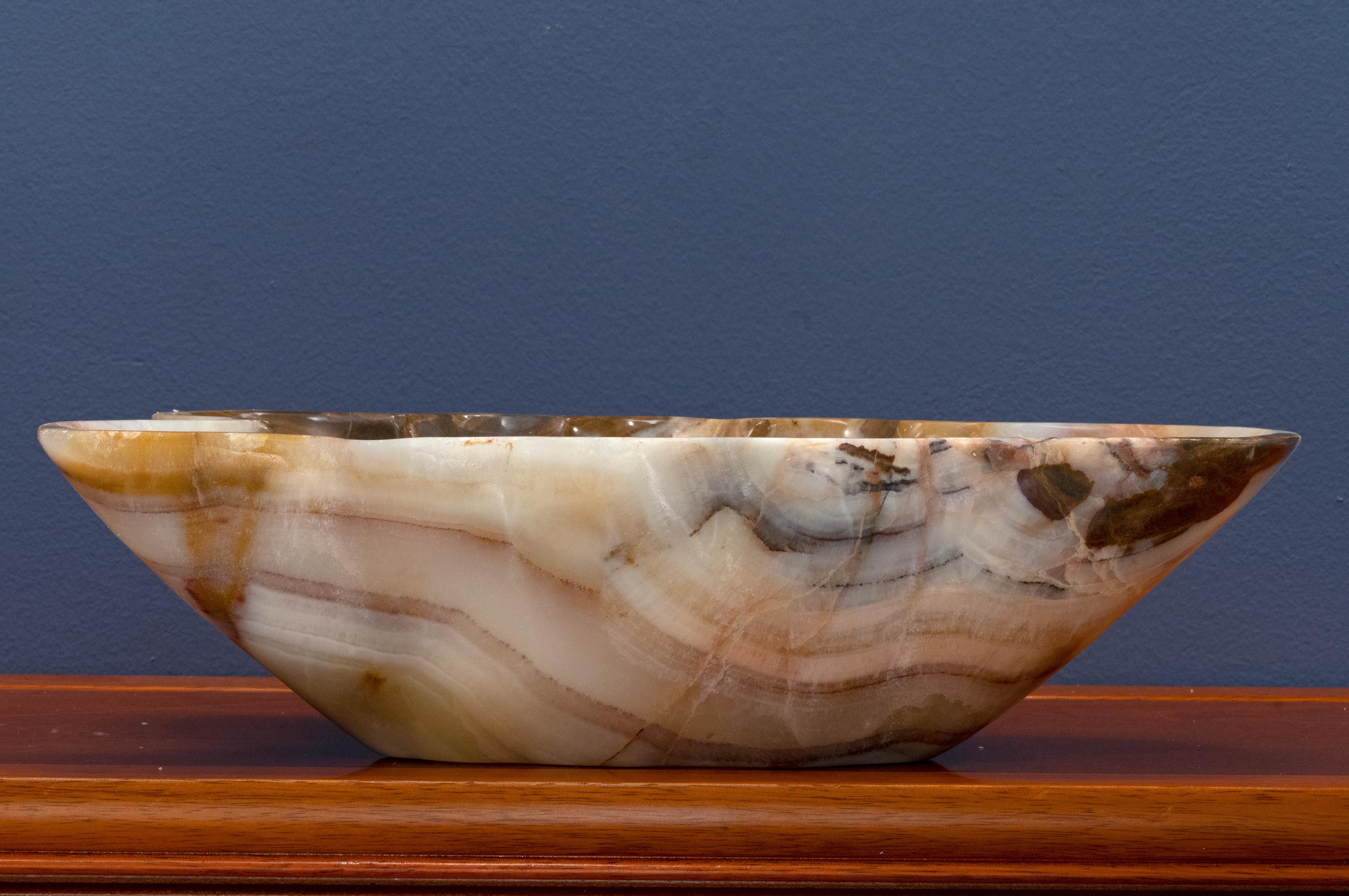 This gorgeously hand-carved and uniquely-shaped 8 pound genuine banded onyx freeform bowl from Pakistan features rich cream and brown banding. This dynamic bowl – the perfect size for a centerpiece – has been hand-polished to a handsome luster. A