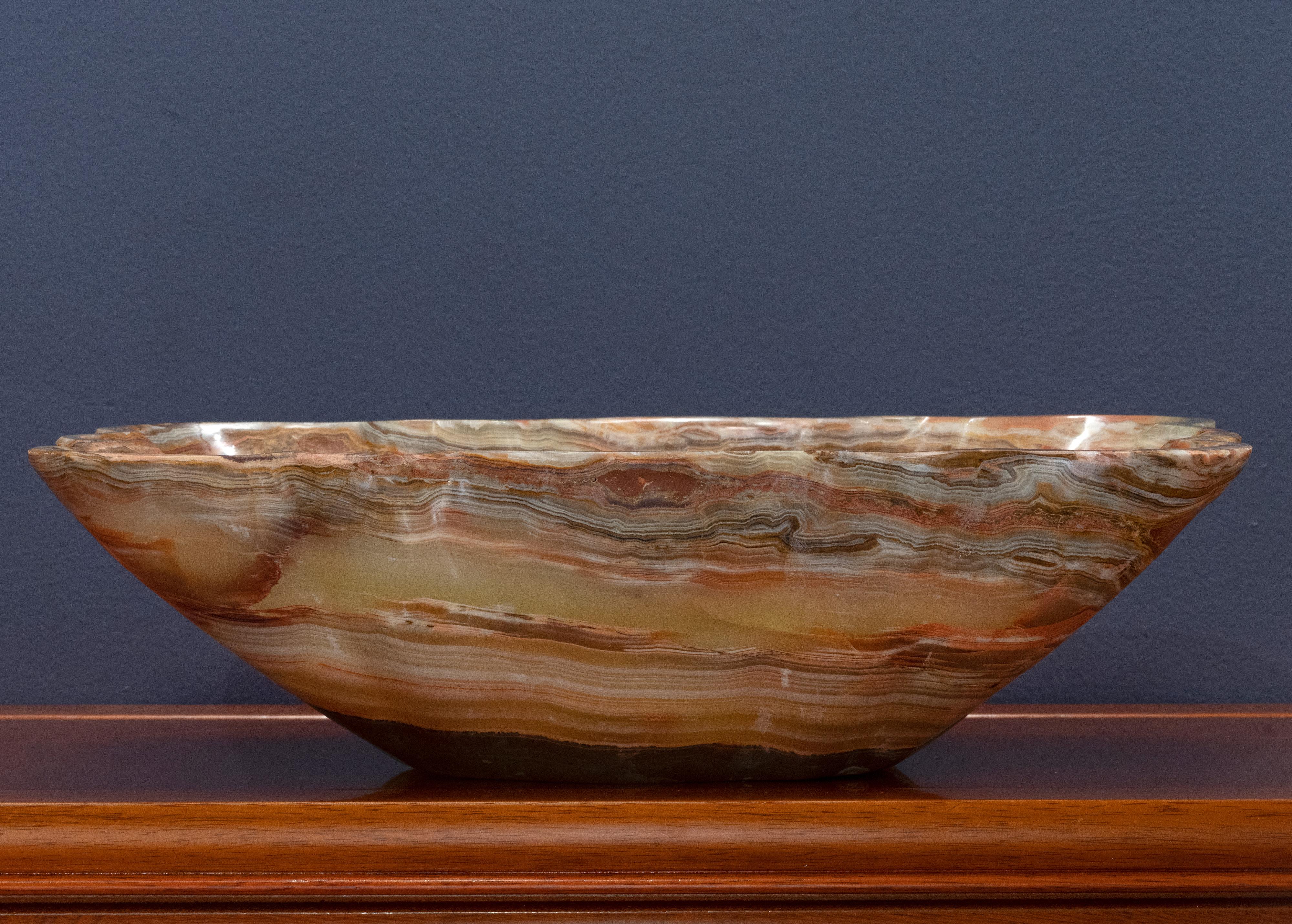 This gorgeously hand-carved 9.5 pound genuine banded onyx scalloped freeform bowl from Pakistan features richly pigmented, concentric bands of brown, green, and tan. This dynamic piece – the perfect size for a centerpiece – has been hand-polished to