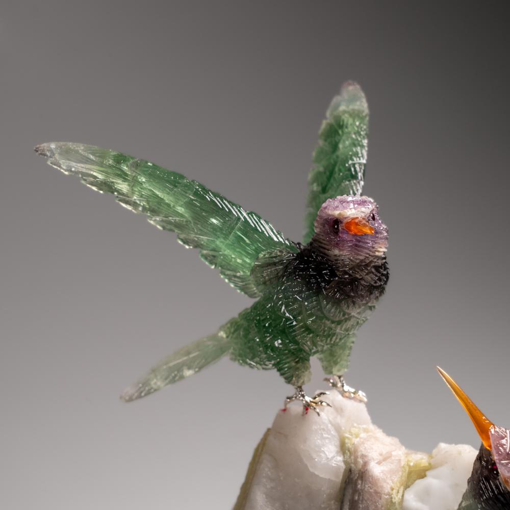 Cette sculpture de colibri est une pièce d'art unique, sculptée dans de la fluorine de qualité musée, avec des yeux en onyx et un bec en cornaline. Le hibou est perché au sommet d'une matrice de tourmaline verte et de quartz et monté sur un support