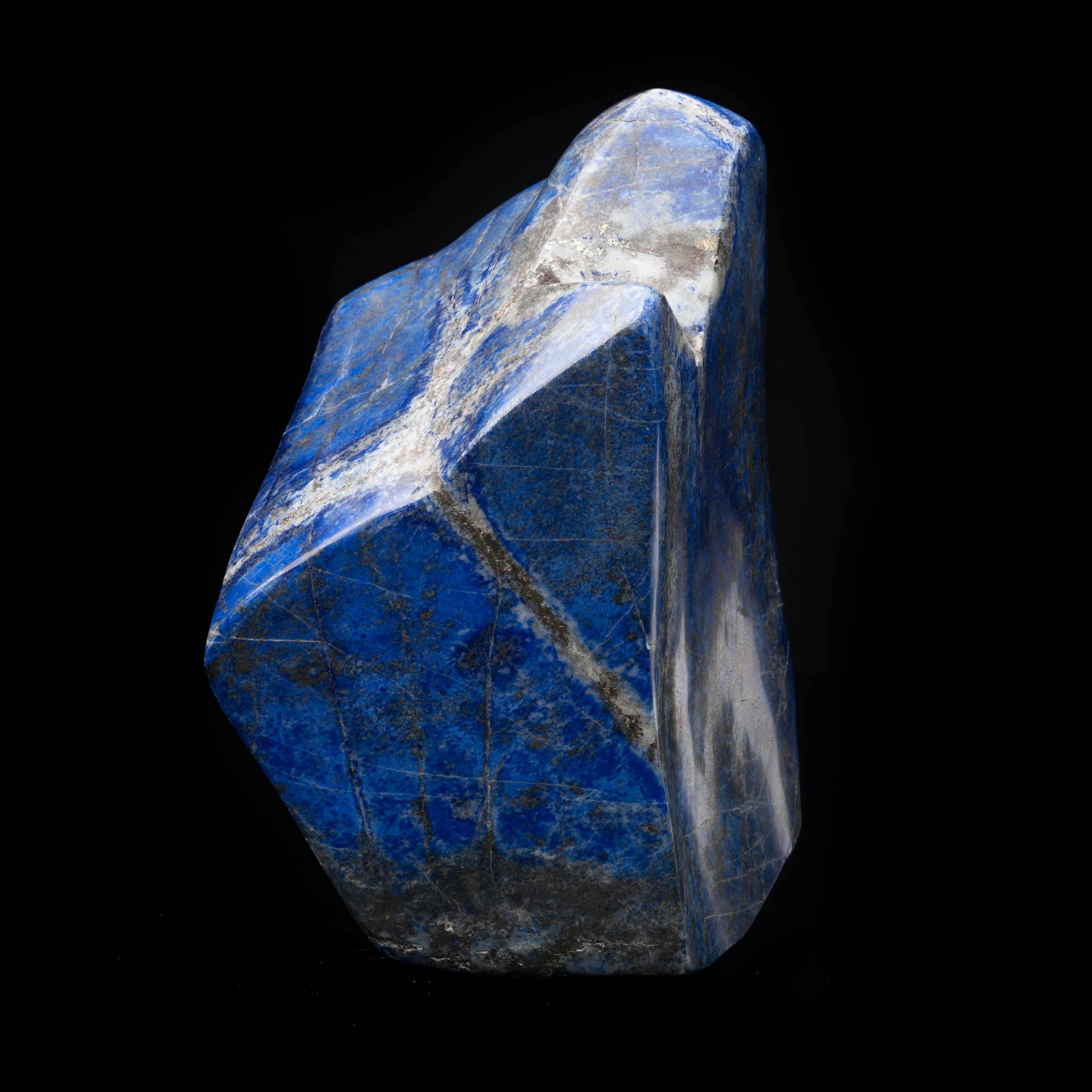 This large hand-polished lapis lazuli freeform features a unique, sculptural shape as well as copious deposits of shimmering pyrite and contrasting veins of white calcite running through the deeply pigmented blue backdrop, creating a beautiful