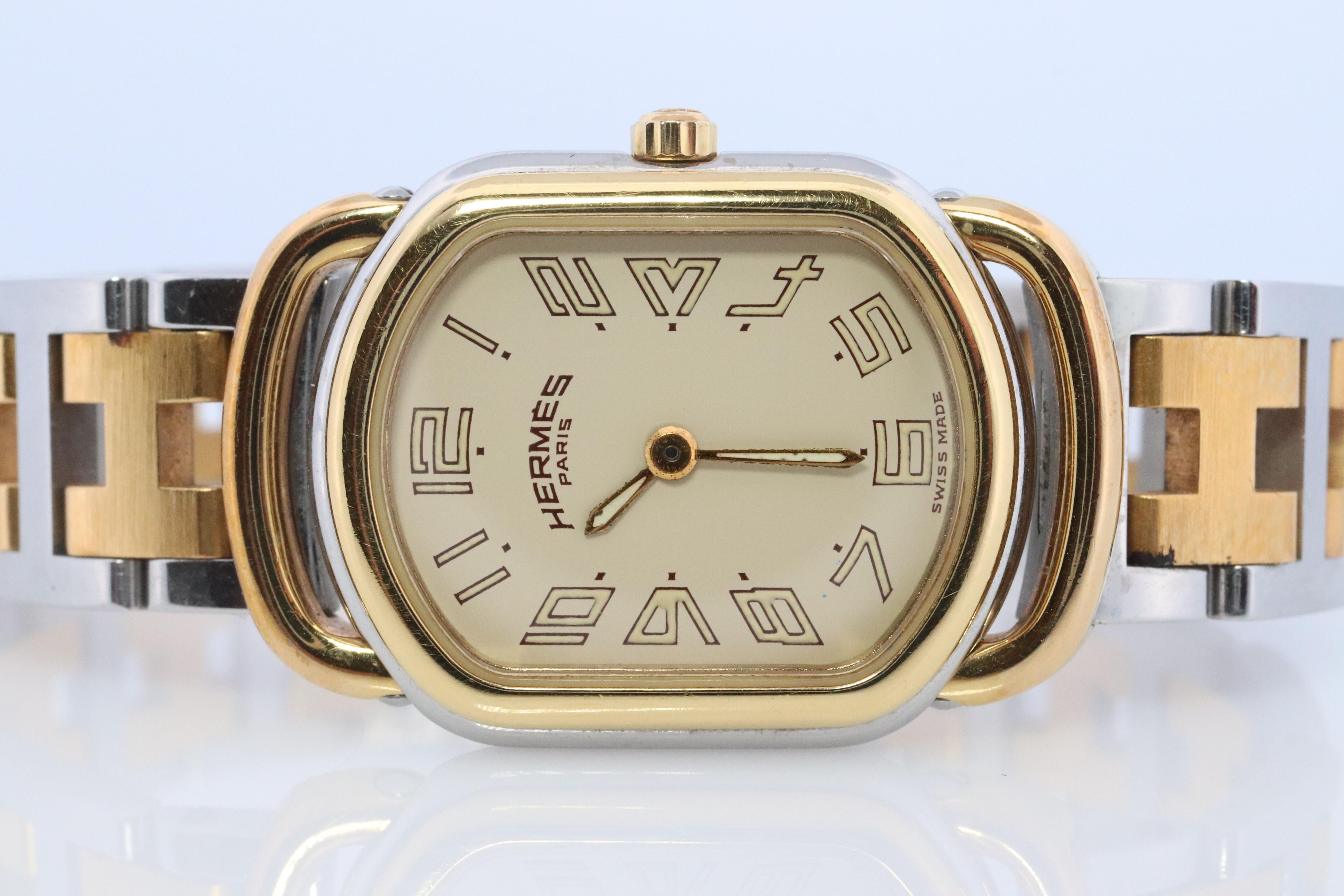 Ceci est une authentique montre HERMES en acier inoxydable 21mm par 29mm Rectangle Rallye Quartz Blanc. La montre est fabriquée en acier inoxydable et présente un cadran champagne, des aiguilles et des index dorés, un bracelet à maillons bicolore,