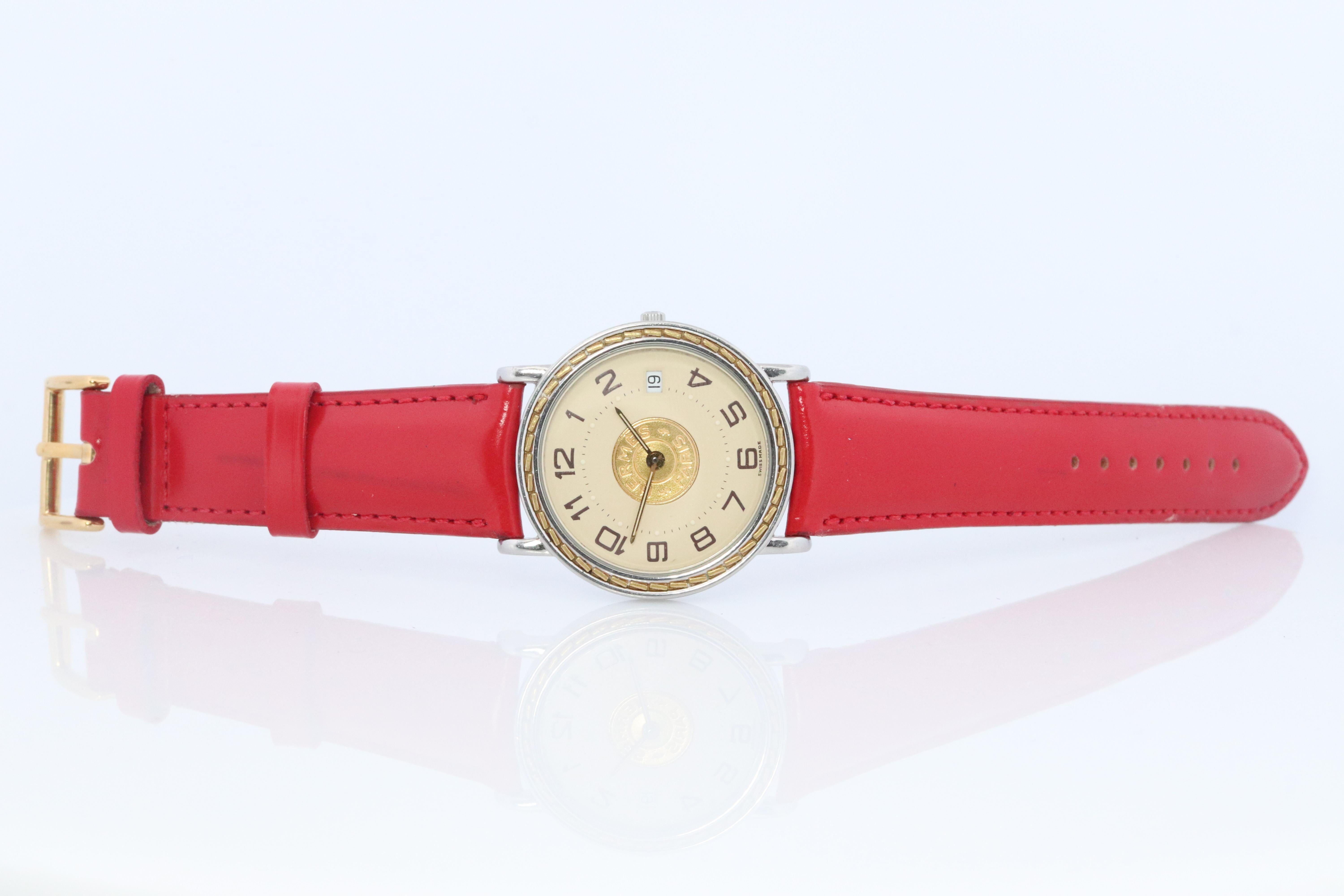 This is an authentic HERMES Stainless Steel 32mm Round Sellier Quartz White Dial with calendar.

The watch is crafted of stainless steel and features a white dial, gold hands and black markers, two tone link bracelet, sapphire crystal, and a quartz