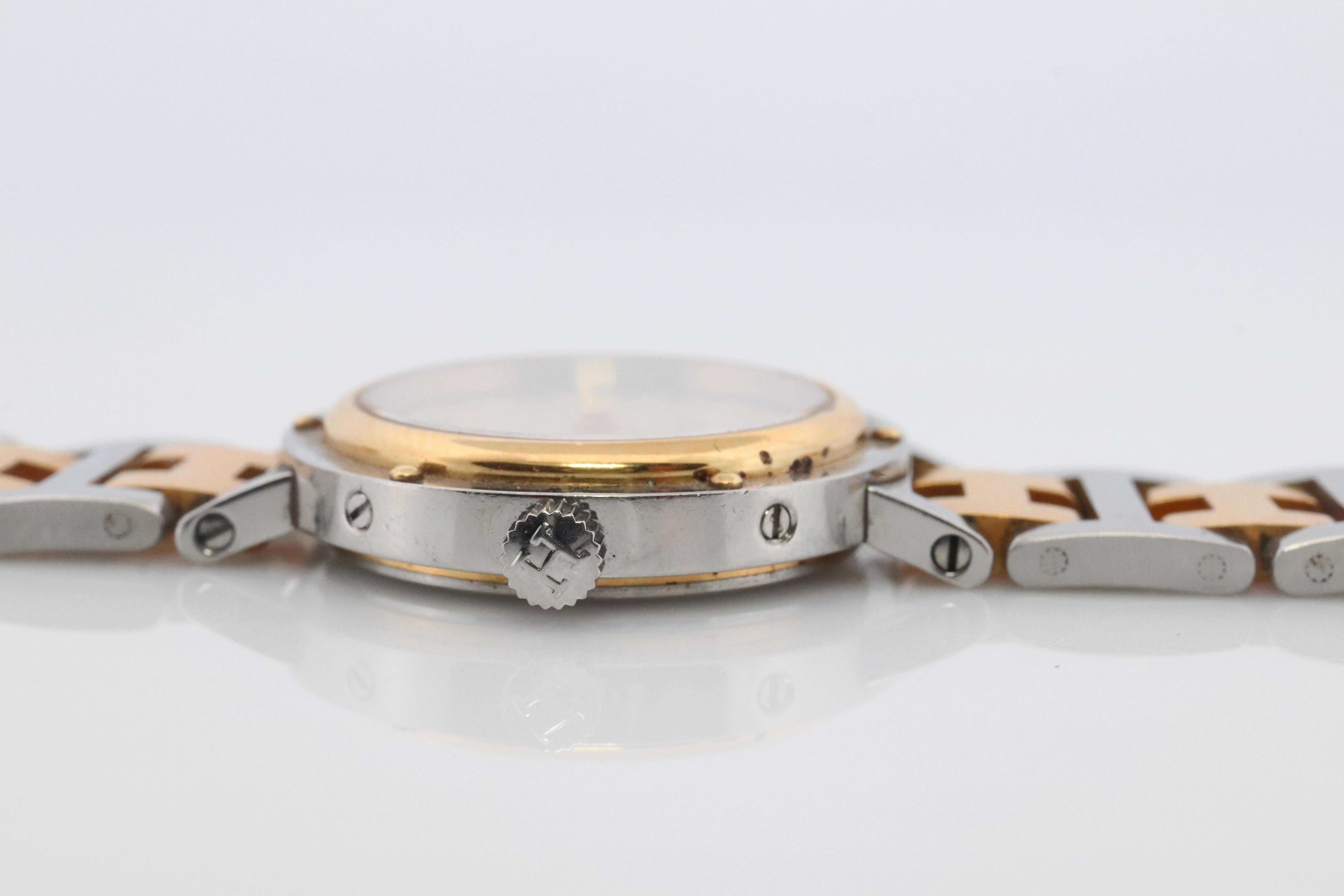 This is an authentic HERMES Stainless Steel Watch

ref CL4.220
24mm Round Clipper 
Quartz 
Champagne Dial. 

The watch is crafted of stainless steel and features a white dial, gold hands and hour markers, two tone link bracelet, sapphire crystal,