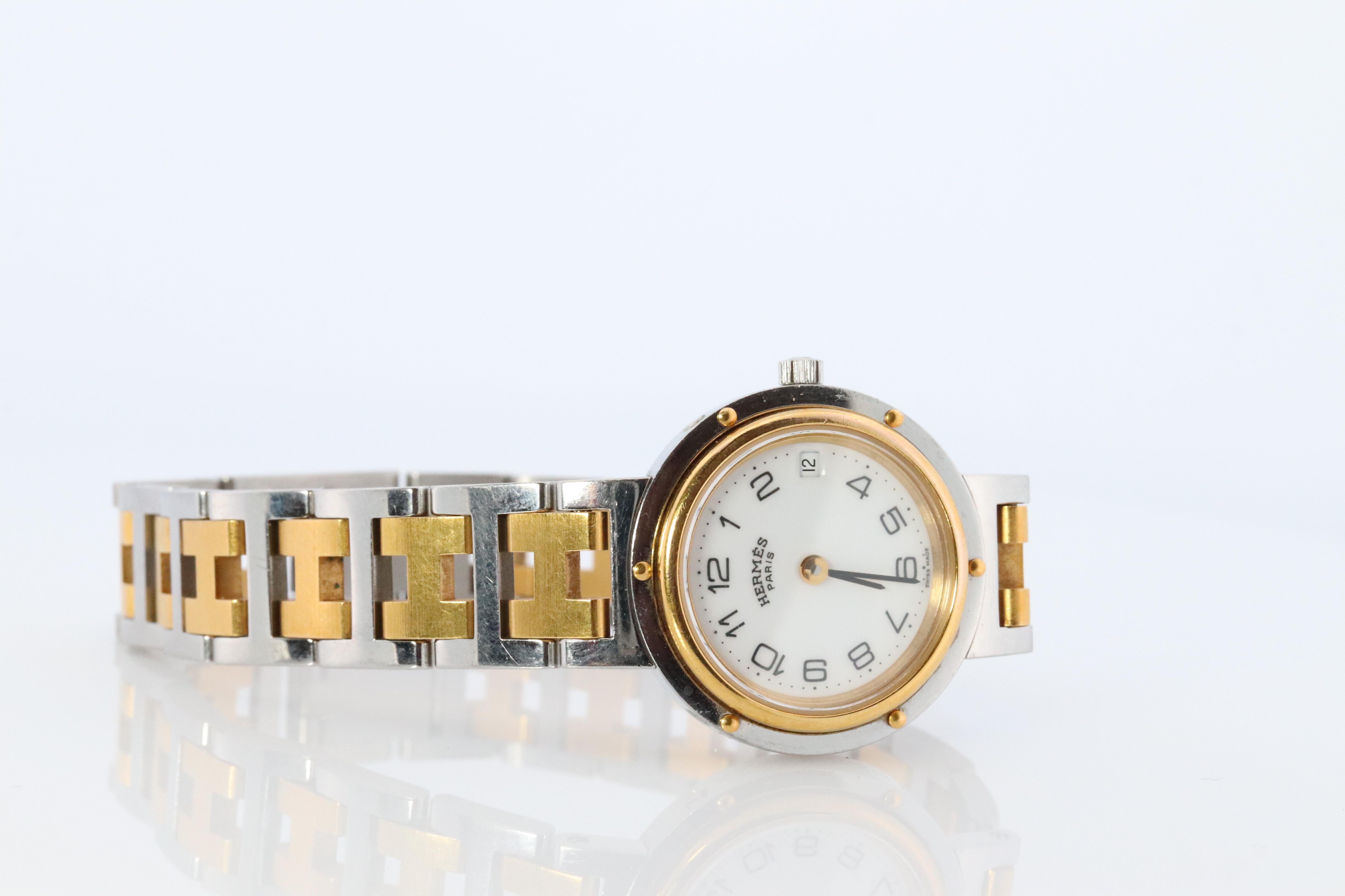 This is an authentic HERMES Stainless Steel 24mm Round Clipper Quartz  White Dial. The watch is crafted of stainless steel and features a white dial, gold hands and hour markers, two tone link bracelet, sapphire crystal, and a quartz movement.

ref