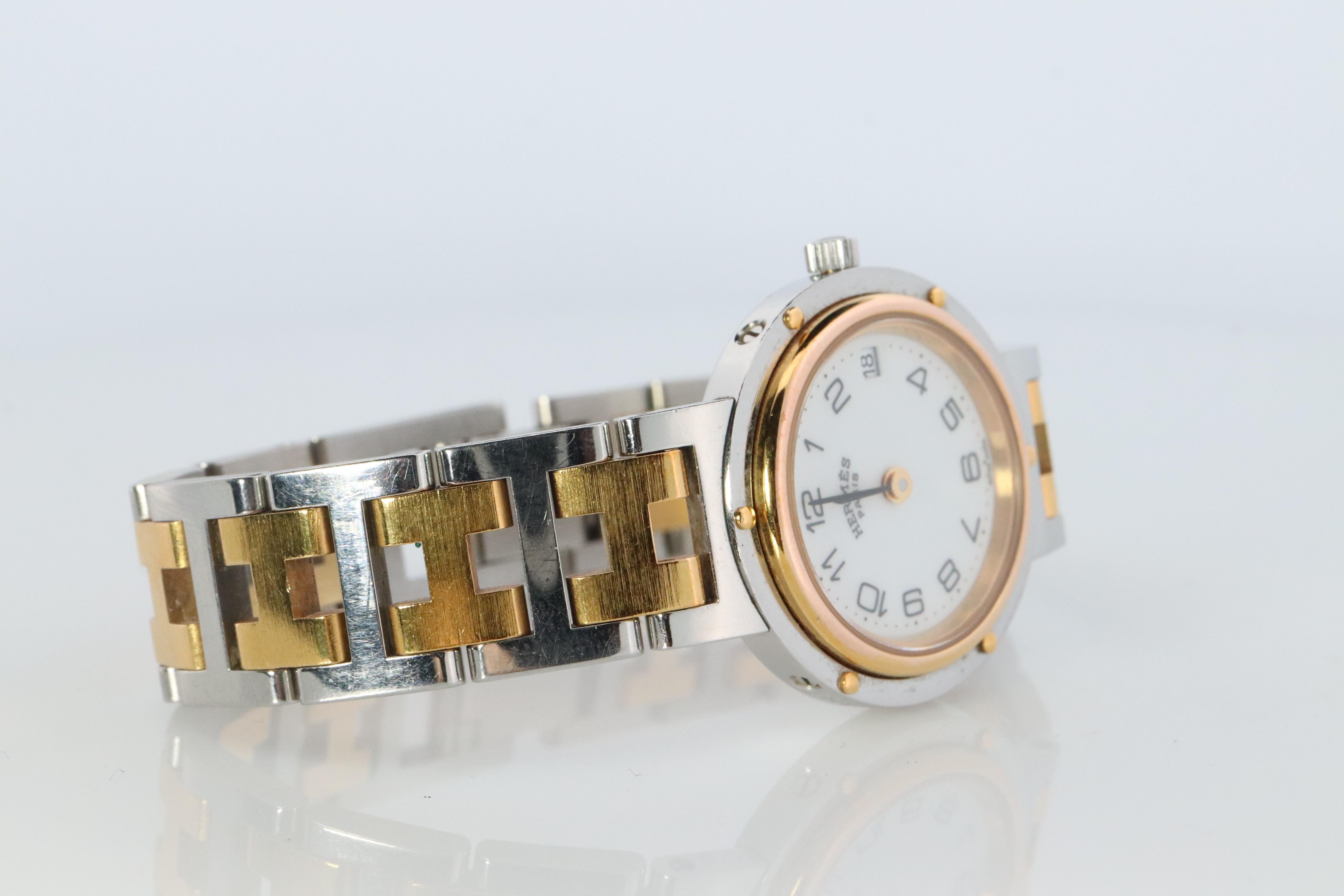 This is an authentic HERMES Stainless Steel 24mm Round Clipper Quartz White Dial. The watch is crafted of stainless steel and features a white dial, gold hands and hour markers, two tone link bracelet, sapphire crystal, and a quartz movement.

ref