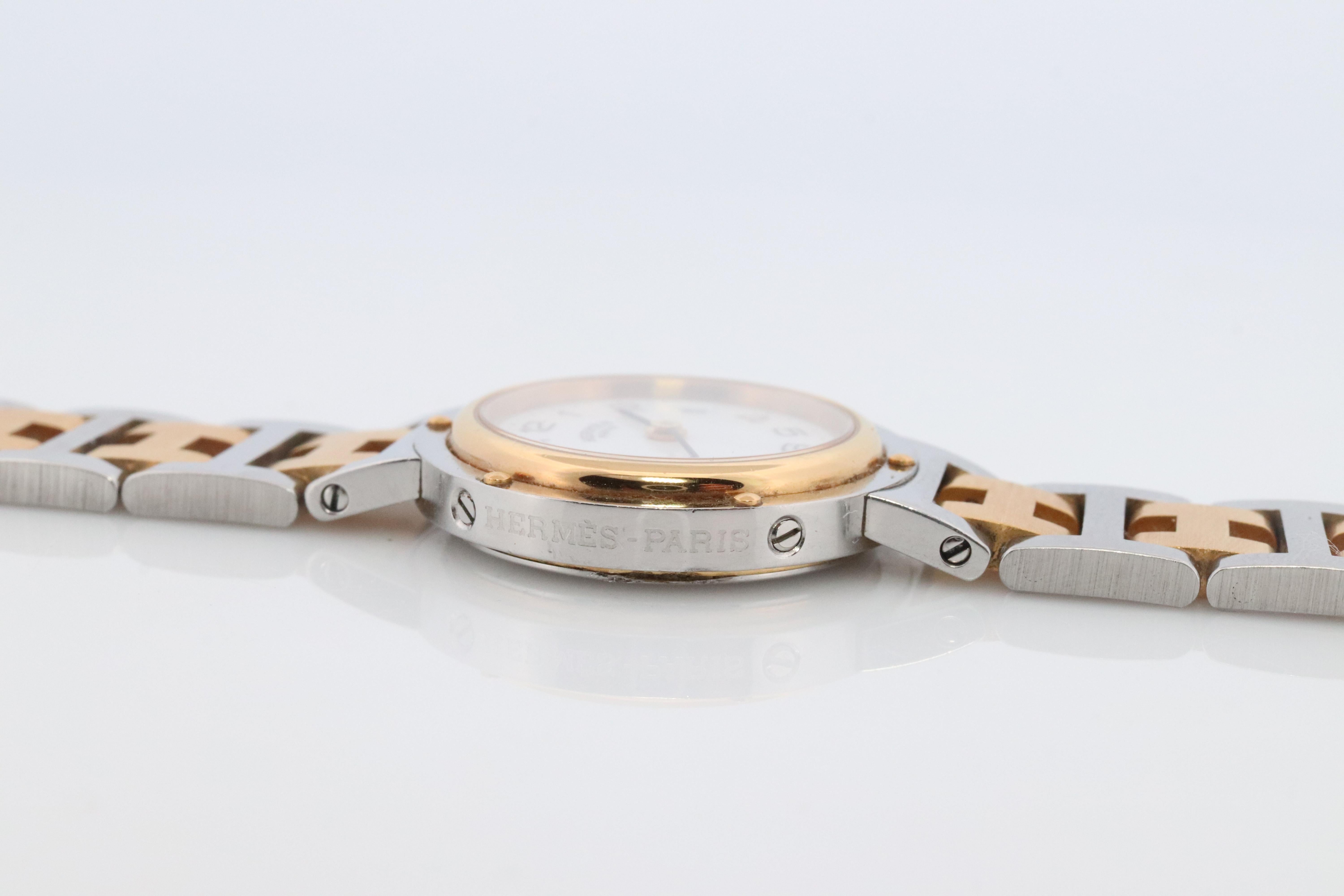 This is an authentic HERMES Stainless Steel Watch

ref CL4.220
24mm Round Clipper 
Quartz 
White Dial. 

The watch is crafted of stainless steel and features a white dial, gold hands and hour markers, two tone link bracelet, sapphire crystal, and a