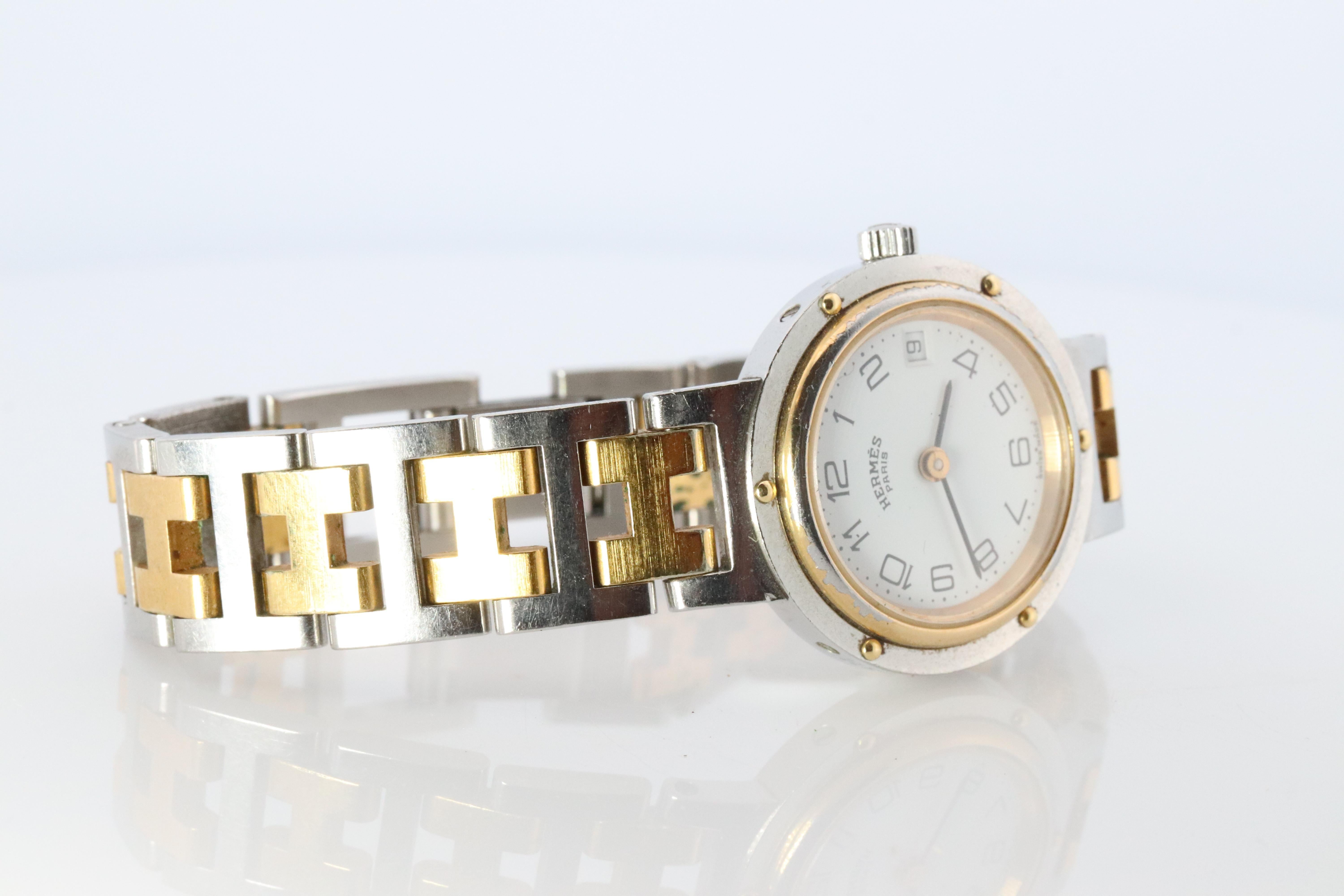 This is an authentic HERMES Stainless Steel Watch

ref CL4.220
24mm Round Clipper 
Quartz 
White Dial. 

The watch is crafted of stainless steel and features a white dial, gold hands and hour markers, two tone link bracelet, sapphire crystal, and a