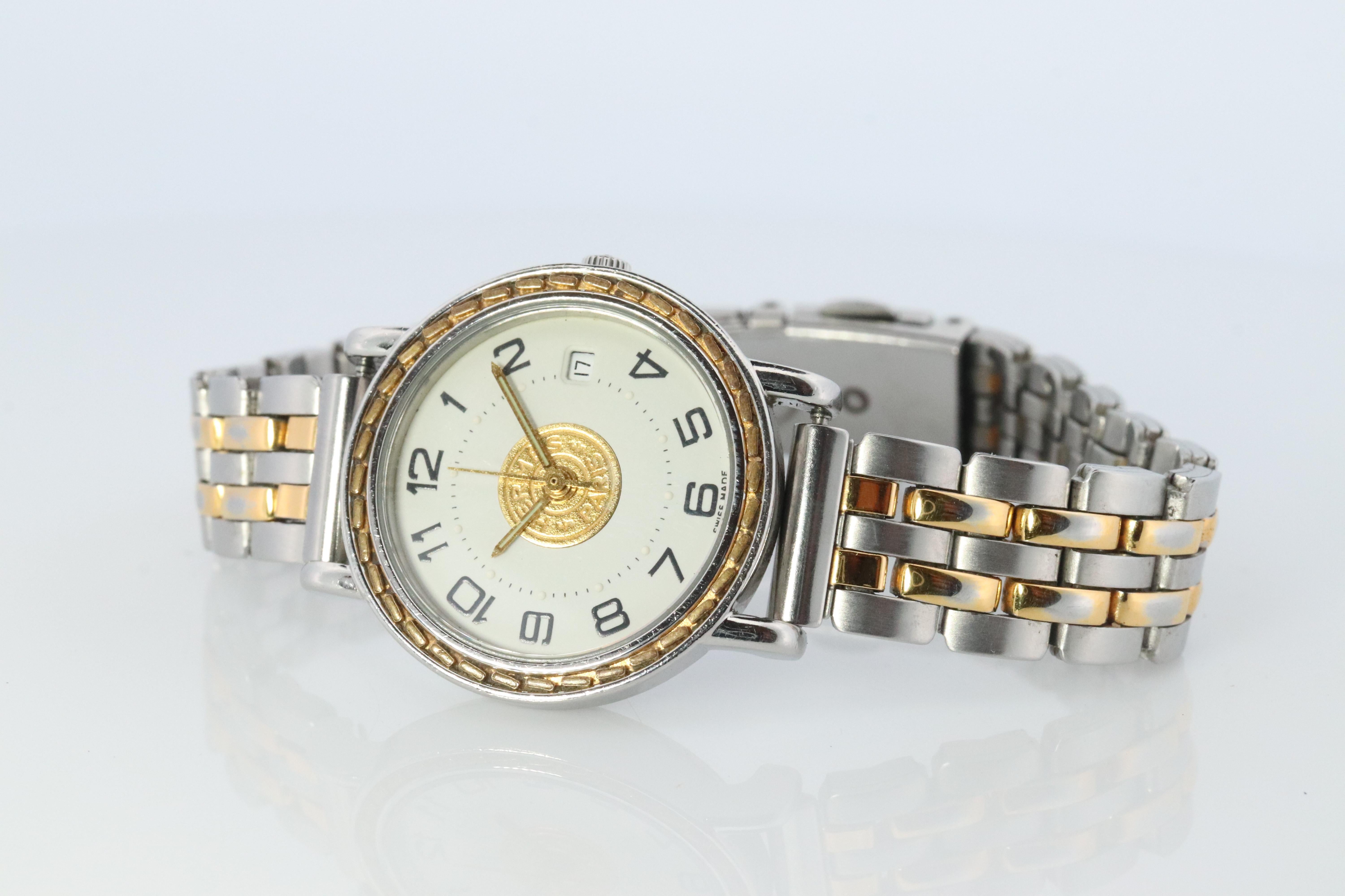 This is an authentic HERMES Stainless Steel 24mm Round Sellier Quartz White Dial. 

The watch is crafted of stainless steel and features a white dial, gold hands and black markers, two tone link bracelet, sapphire crystal, and a quartz