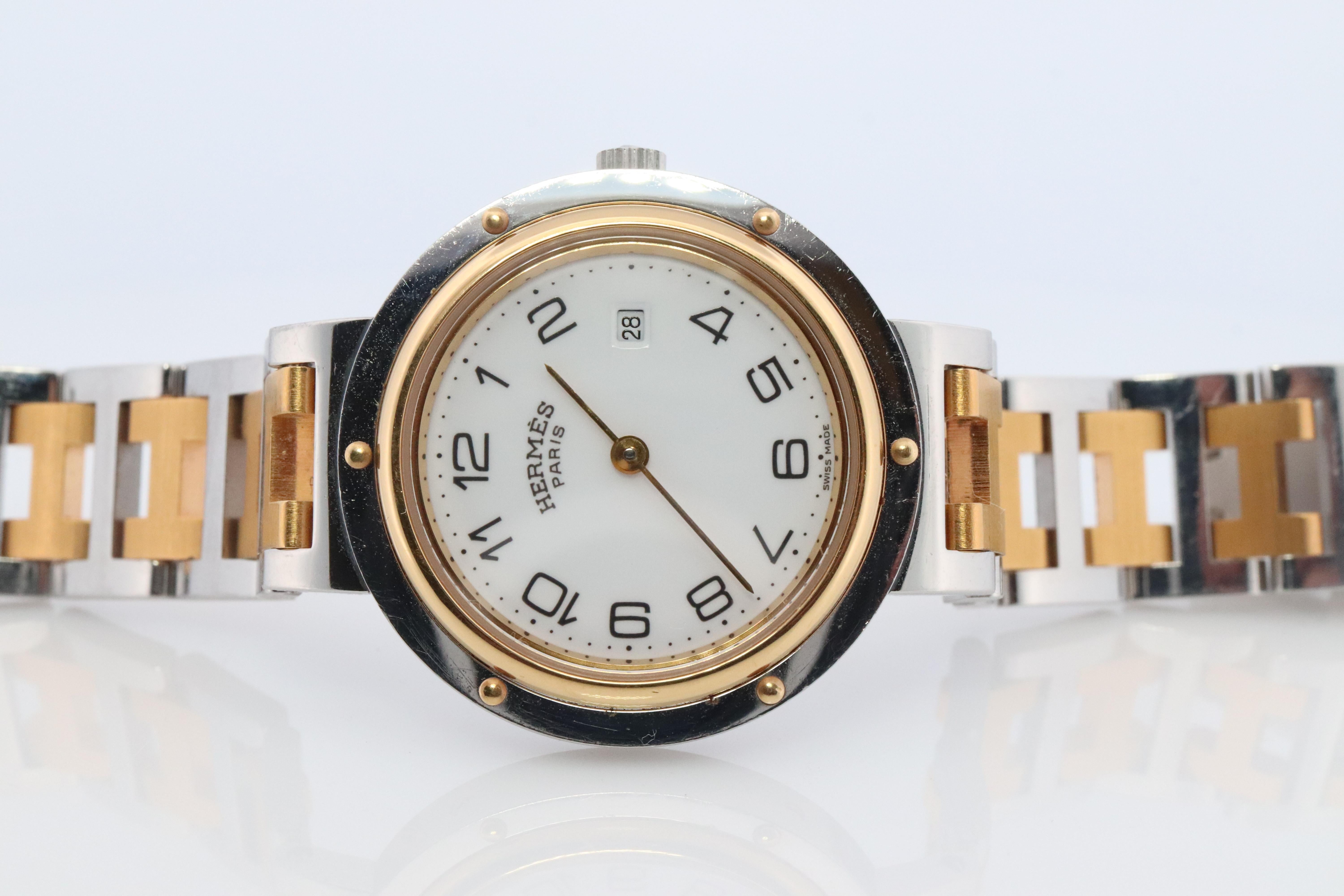 This is an authentic HERMES Stainless Steel 

30mm Round Clipper 
White Dial.
Quartz  New Battery replaced.

The watch is crafted of stainless steel and features a white dial, gold hands and hour markers, two tone link bracelet, sapphire crystal,