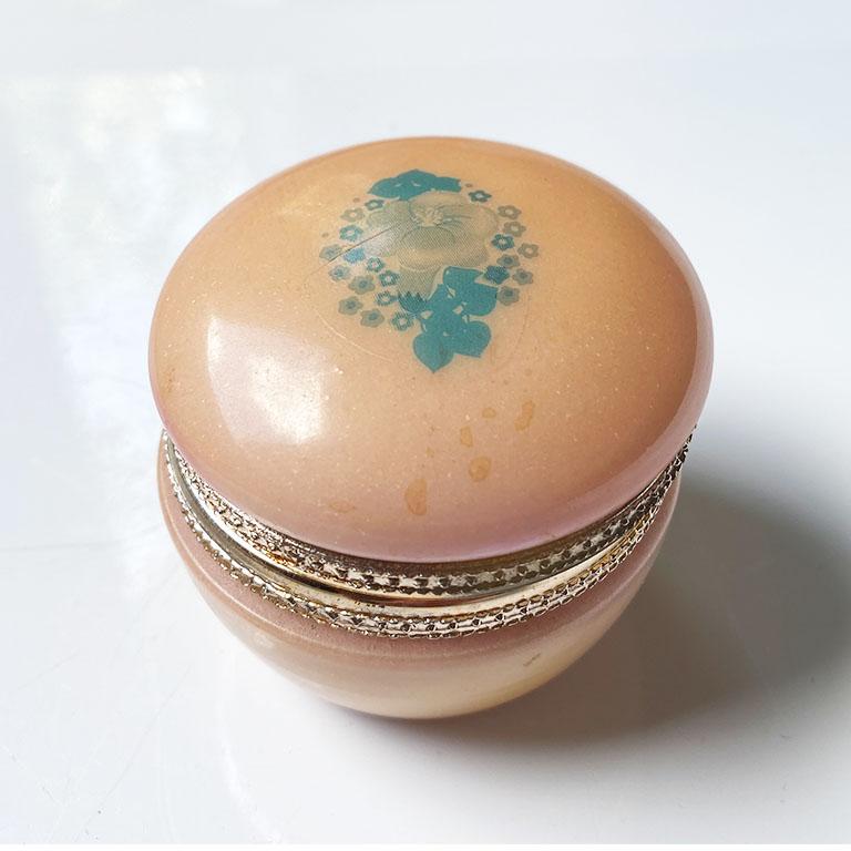 A lovely hand-carved round Italian alabaster or opaline glass trinket box in pink. This piece will be fabulous to display on a coffee table or dressing table. The exterior is a peachy pink color. Its hinged lid is in gold and lifts up to reveal the