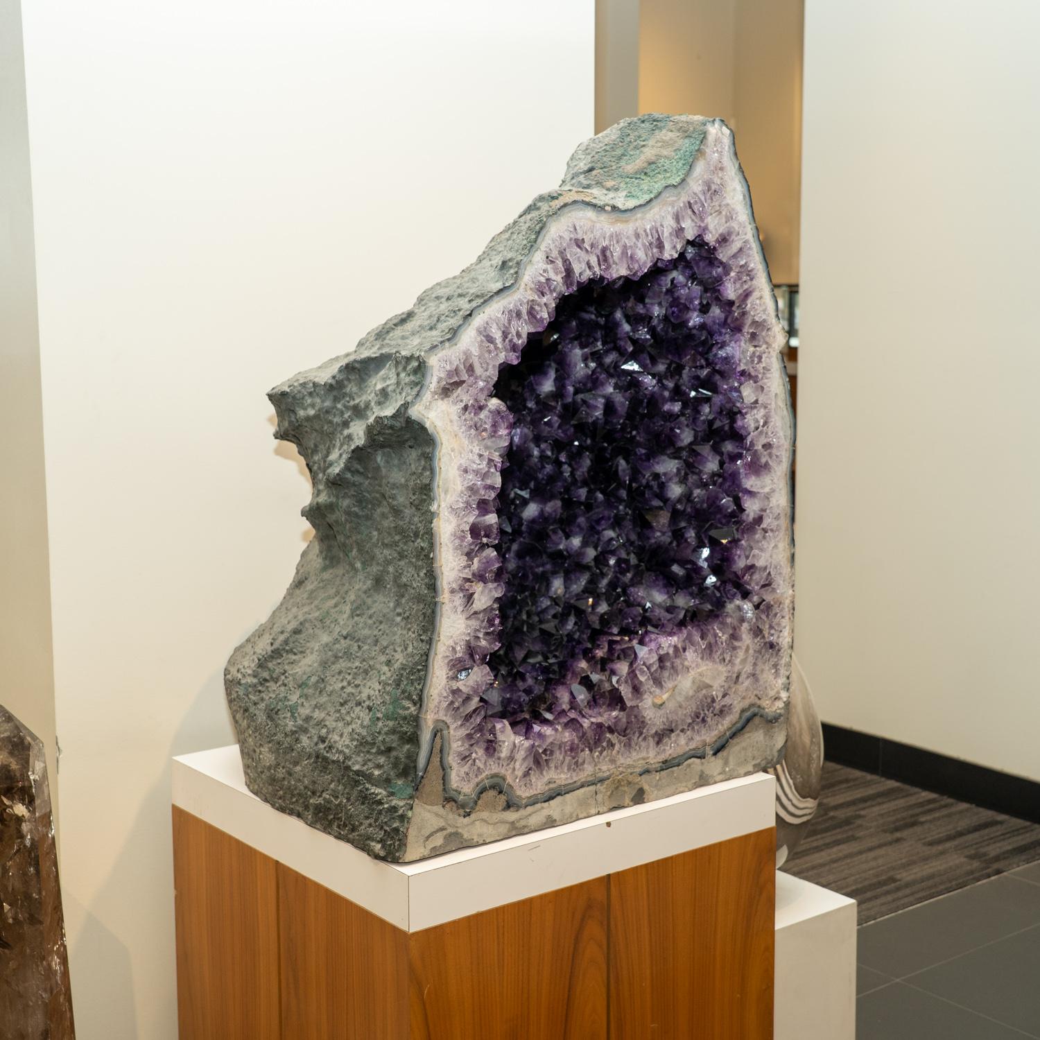 Esta Geoda de Racimo de Amatista auténtica de Brasil es una formación natural de amatista gema de primera calidad acentuada por pequeños cristales planos de calcita. La decoración de media geoda catedral presenta lustrosos cristales totalmente