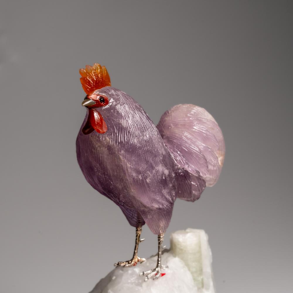 Diese Hahnschnitzerei ist ein einzigartiges Kunstwerk, geschnitzt aus Amethyst in Museumsqualität mit Augen aus Karneol. Der Hahn sitzt auf einem grünen Turmalin in einer Quarz-Matrix und ist auf einem speziell angefertigten Ständer montiert, um ihn