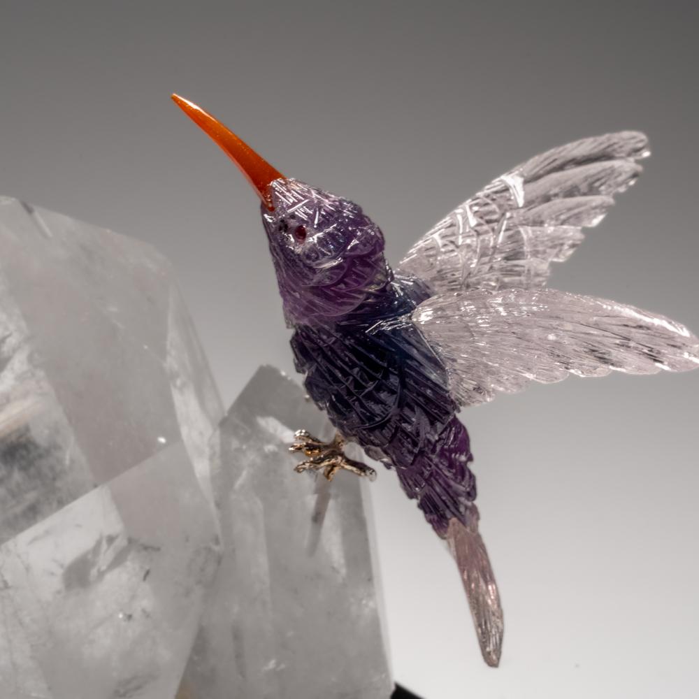 This Hummingbird carving is a unique piece of art, carved from museum-quality clear quartz two dolphin, with garnet eyes. The dolphins is perched atop an amethyst geode matrix and mounted on a custom stand for convenient display. This sculpture is