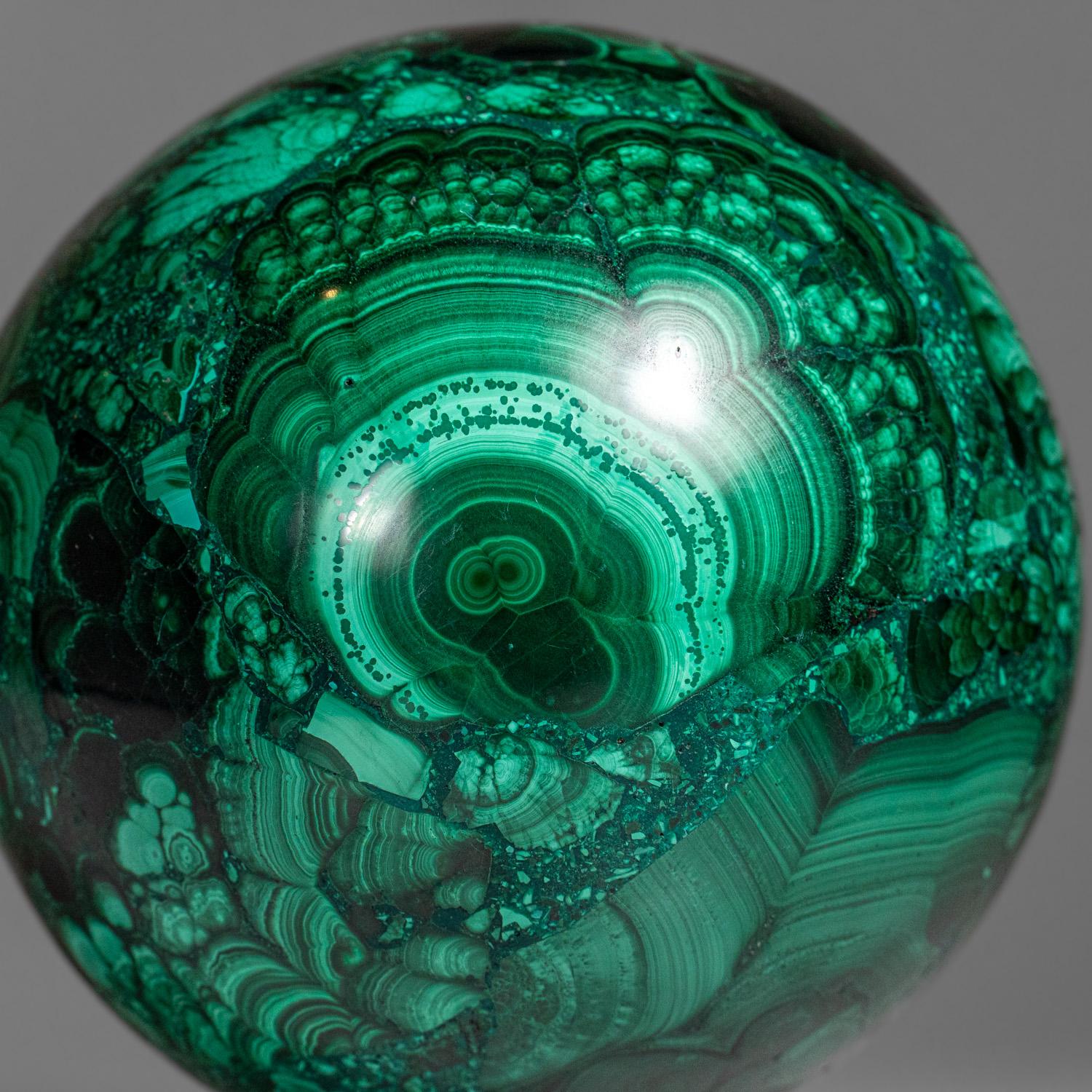 This genuine polished Malachite sphere is sourced from Zaire and features a well-defined green banded pattern. It is solid material with no fill and comes with an acrylic display stand. Known for its balancing and transformative properties,