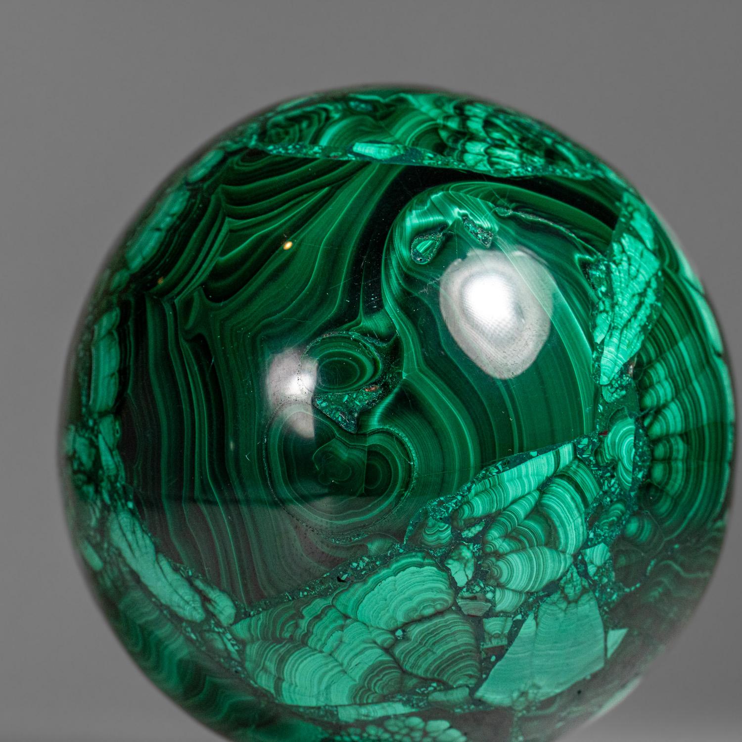 This genuine polished Malachite sphere is sourced from Zaire and features a well-defined green banded pattern. It is solid material with no fill and comes with an acrylic display stand. Known for its balancing and transformative properties,