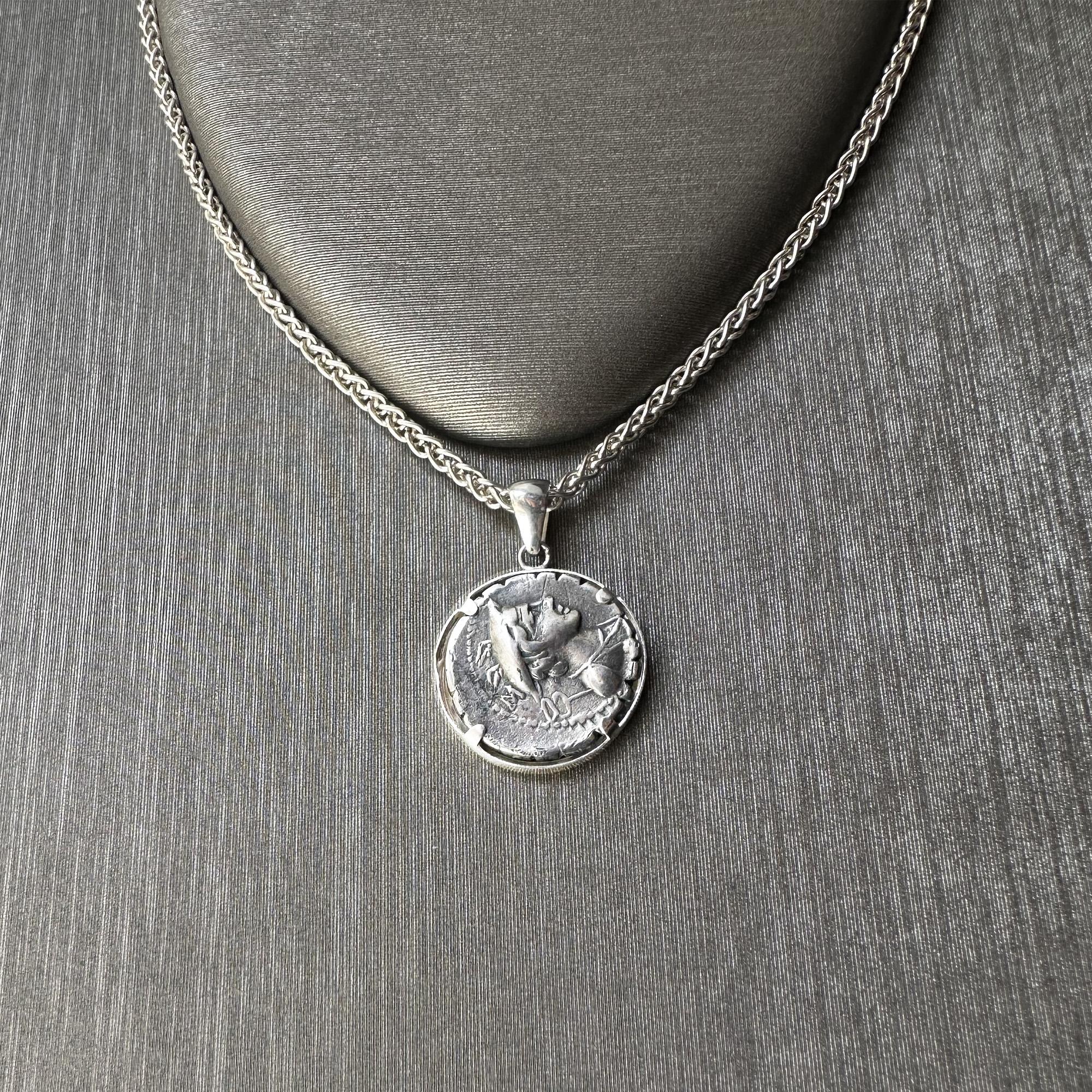 Entdecken Sie einen echten römischen Münzanhänger aus dem Jahr 82 v. Chr., eingefasst in einen Anhänger aus Sterlingsilber. Dieses bemerkenswerte Stück zeigt auf der Vorderseite Ulysses, der seinem treuen Hund Argos die Arme öffnet. Auf der