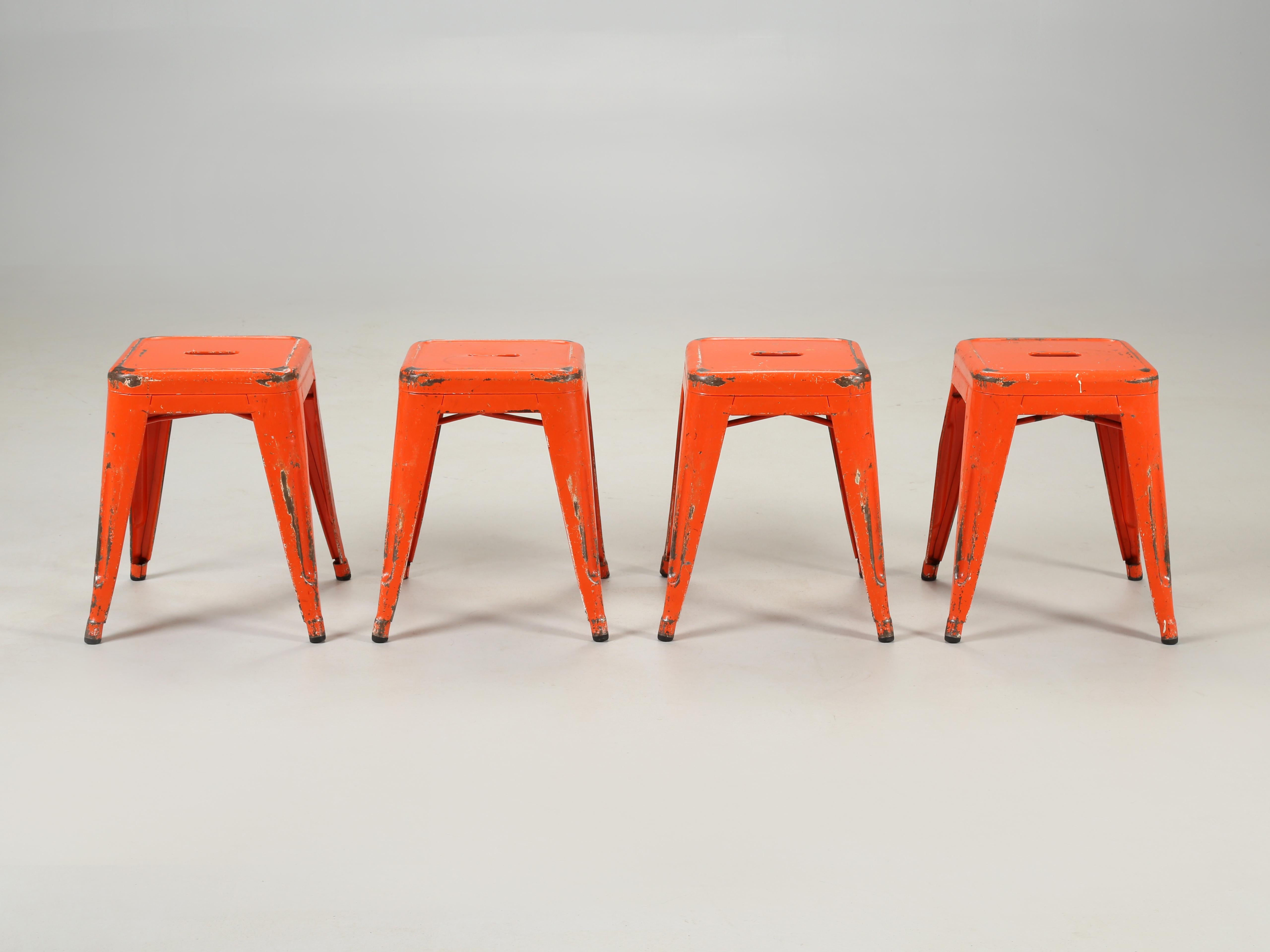 Genuine set of (4) Tolix steel stacking stools probably dating to the 1960's in a vibrant orange and yes, they are heavily distressed. We have hundred's of virtually new showroom samples available in (3) different heights. Dining table height as