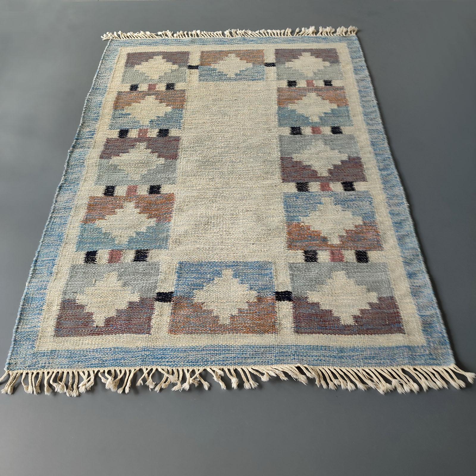 Genuine Vintage Scandinavian Kilim rug, design attributed to Karin Jönsson. 
The color palette comprises of gentle shades of beige, brown and grey, with black and rust pink accents, against a neutral beige background, with faded blue border, in